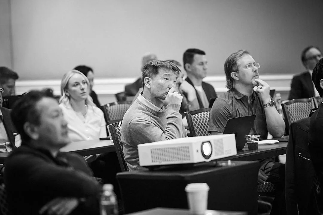 People attending a conference or seminar, sitting at tables and listening attentively.