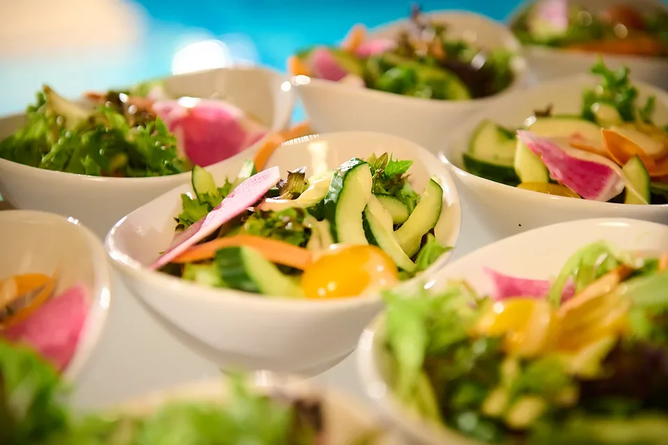Several white bowls filled with fresh vegetable salads, including cucumbers, radishes, cherry tomatoes, and leafy greens.