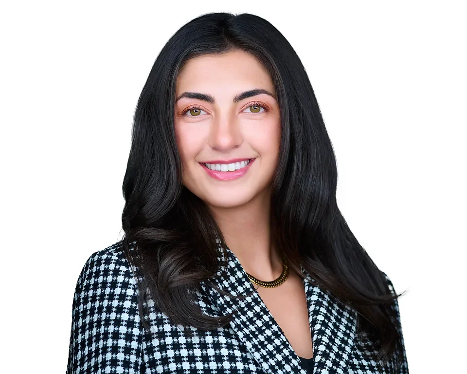 A young woman with long black hair, smiling and wearing a black and white checkered blazer, gold necklace, and a black top