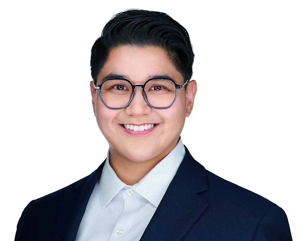 A young man with black hair, glasses, and a suit smiling against a white background.