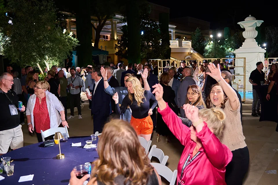 People dancing and socializing at an outdoor night event with string lights and decorative elements in the background.