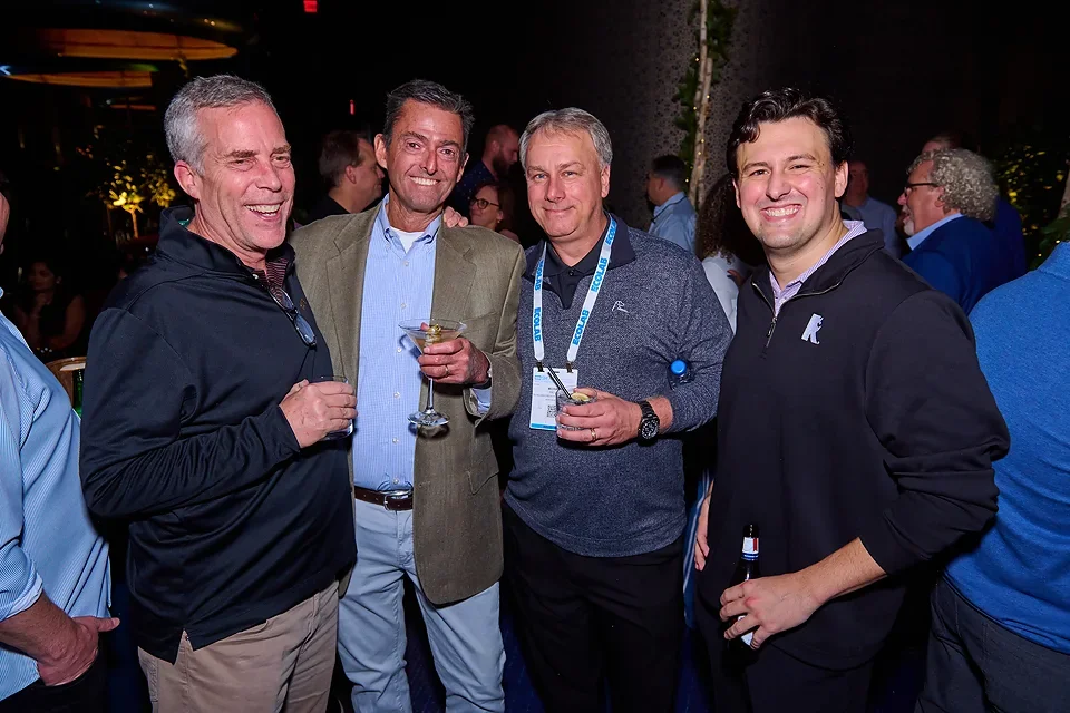 Four men smiling and holding drinks at a social event or party.