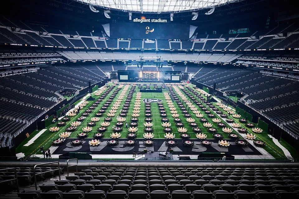 Empty indoor stadium with rows of tables and chairs arranged on the field, likely for an event or celebration.