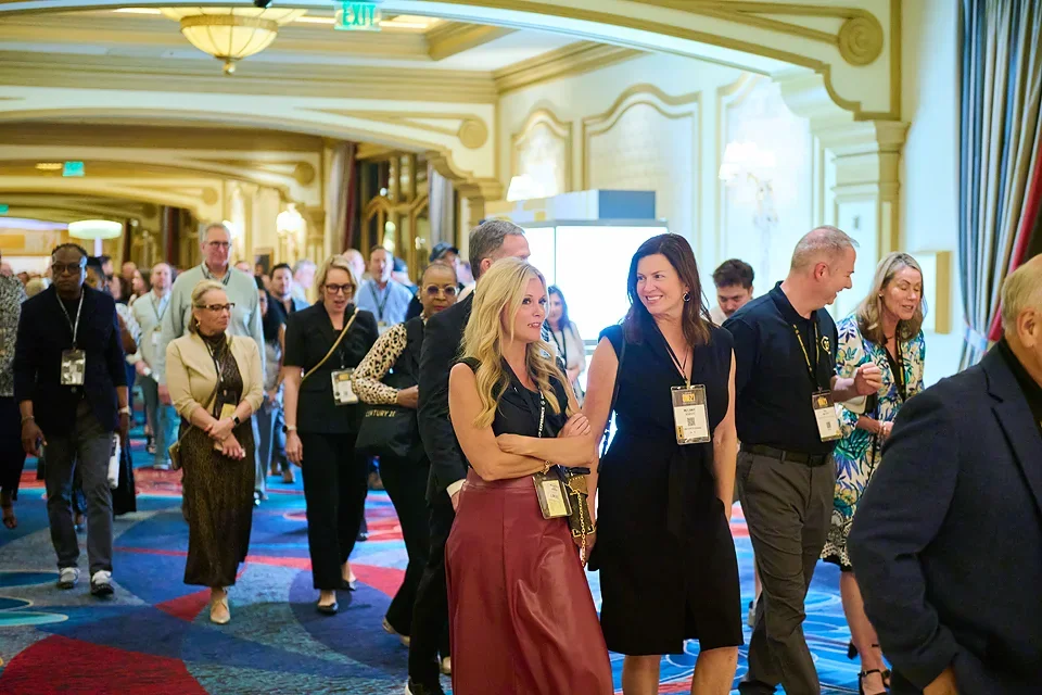 People attending a conference or event in an elegant hotel lobby, walking in a line, wearing name badges, with a bright and ornate interior.