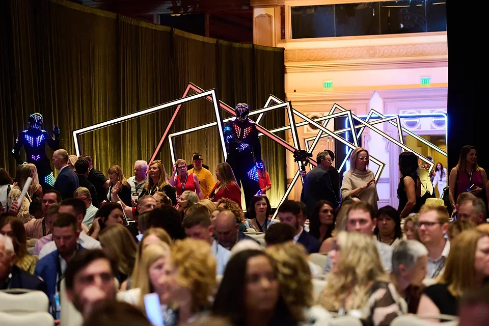 Crowd of people at an indoor event with futuristic LED light sculptures and robots in the background.