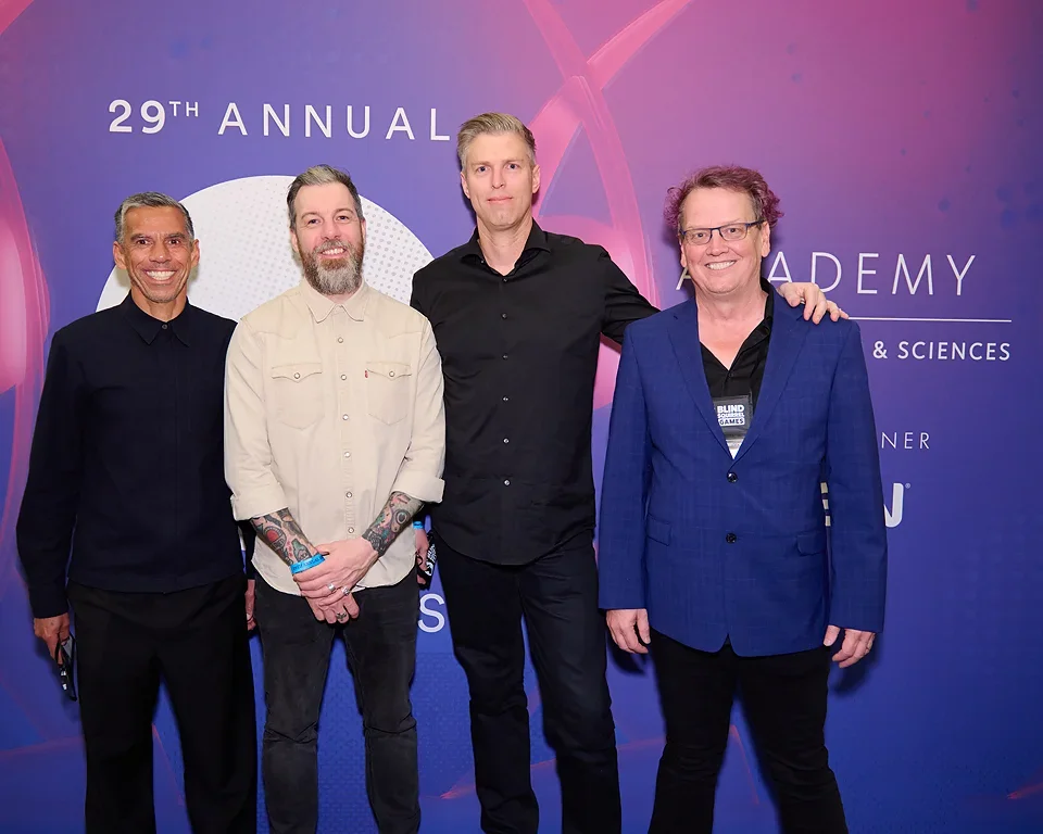 Four men standing together at a conference or event with a purple and pink backdrop that says '29th Annual Academy.'