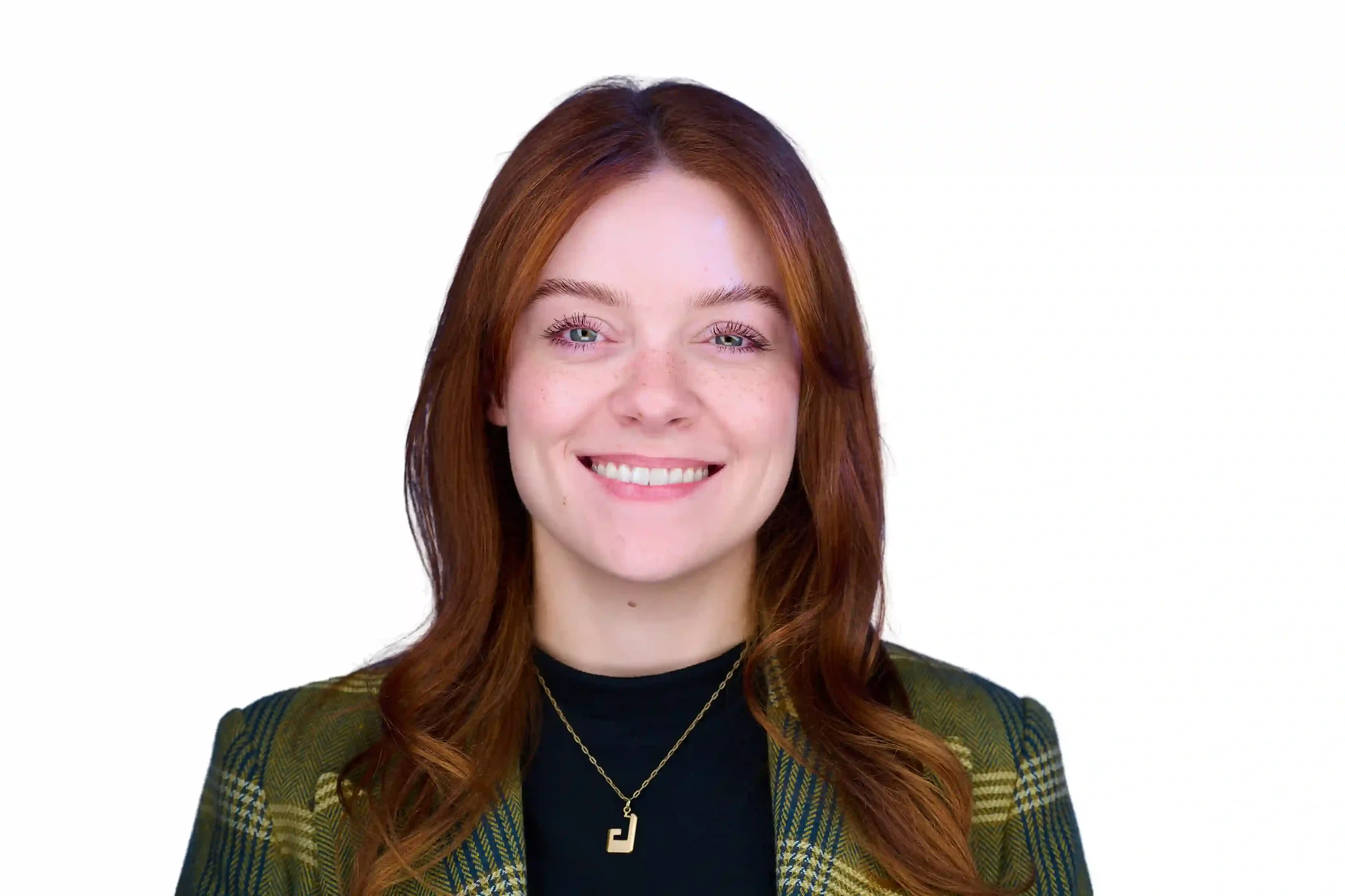 Smiling young woman with red hair, blue eyes, wearing a black top, a plaid blazer, and a gold necklace with a pendant, against a white background.