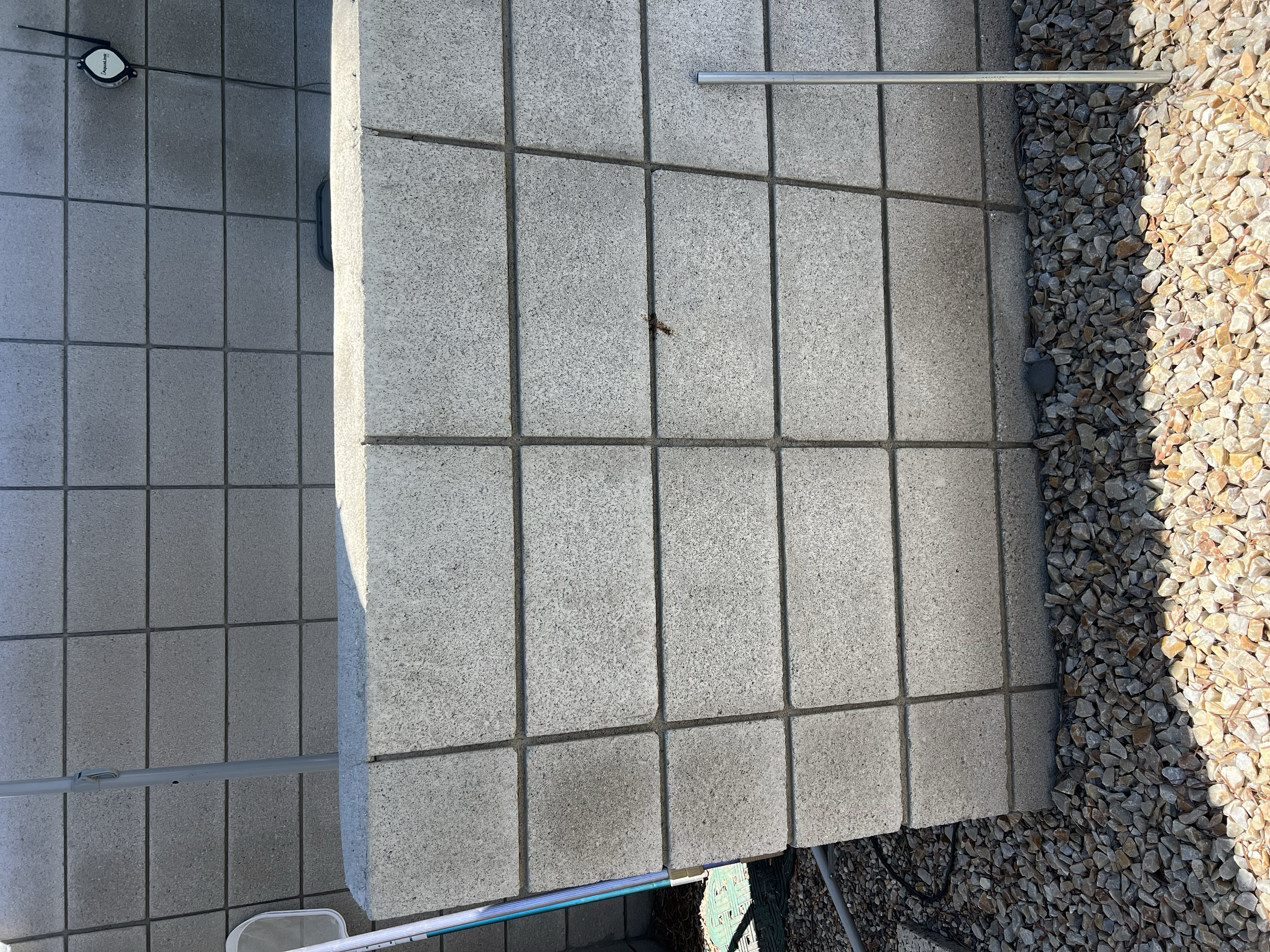 Concrete steps with tiled surface, metal railing, and gravel surroundings.