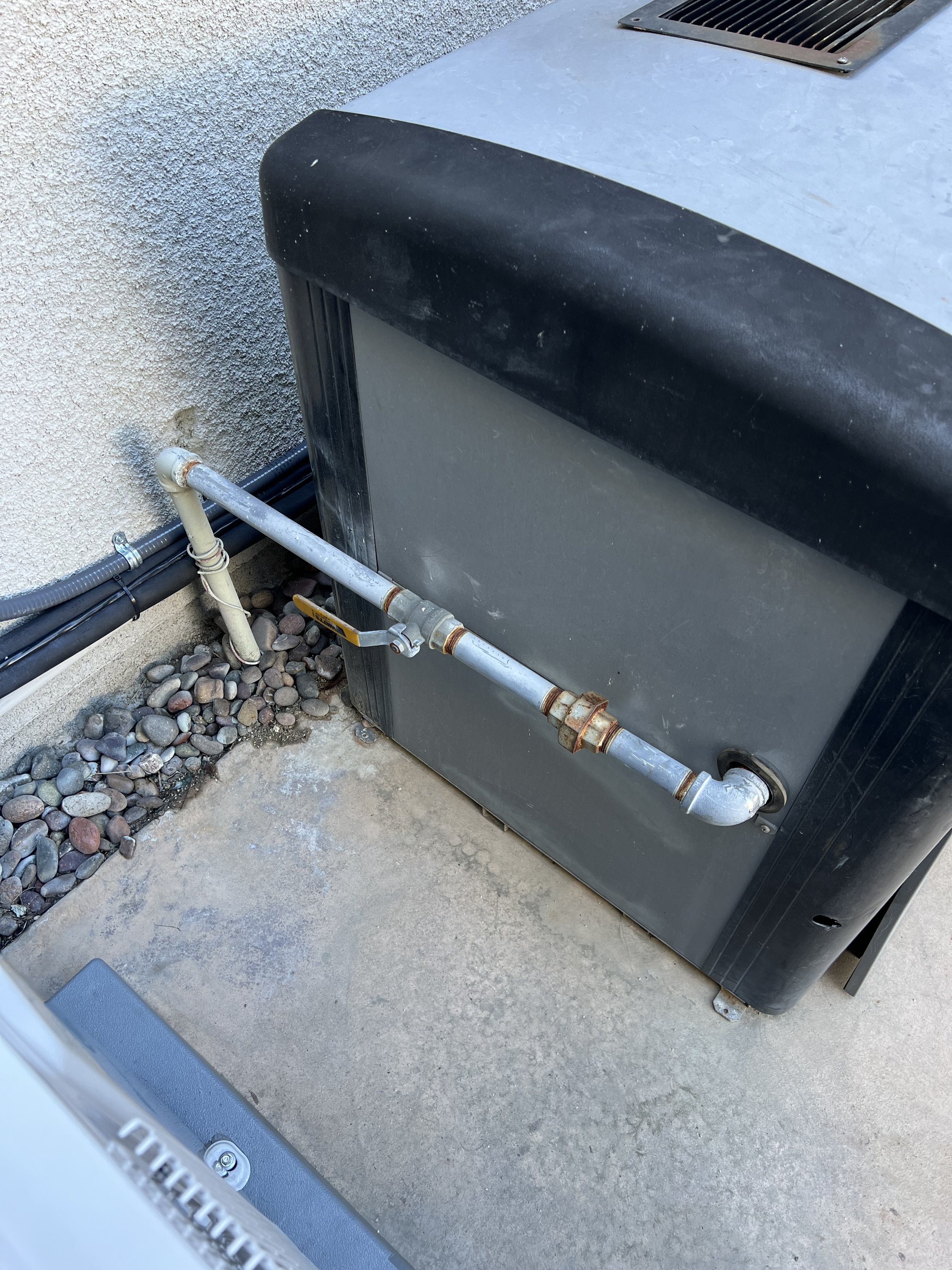Outdoor pool heater unit with connected piping and visible pebbles on the ground.