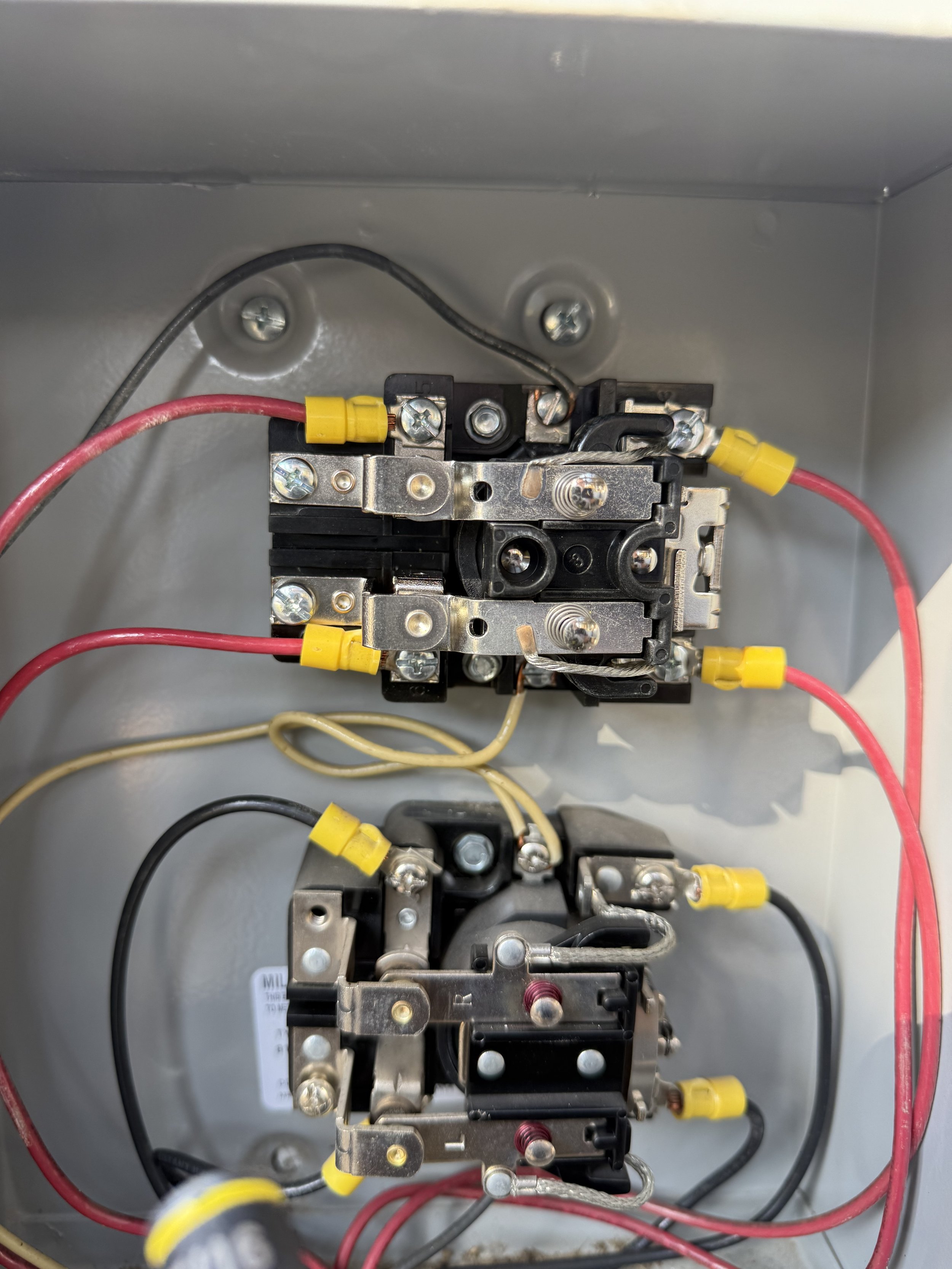 Electrical contactors with yellow and red wires inside a metal enclosure.