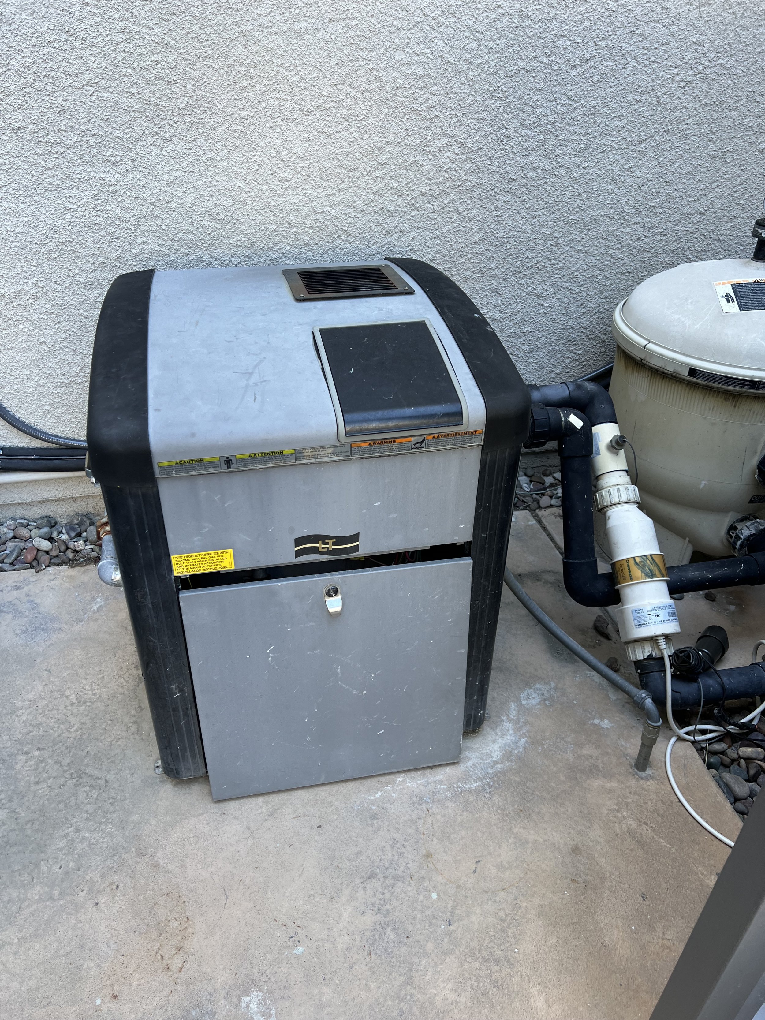 Pool heater next to filter and pipes on concrete ground.