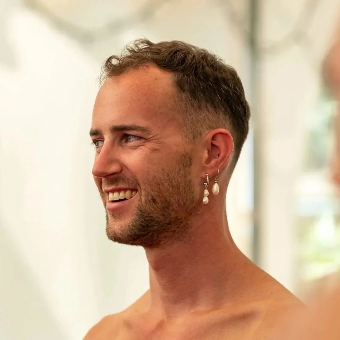 A smiling man with short brown hair and earrings, looking to the right.