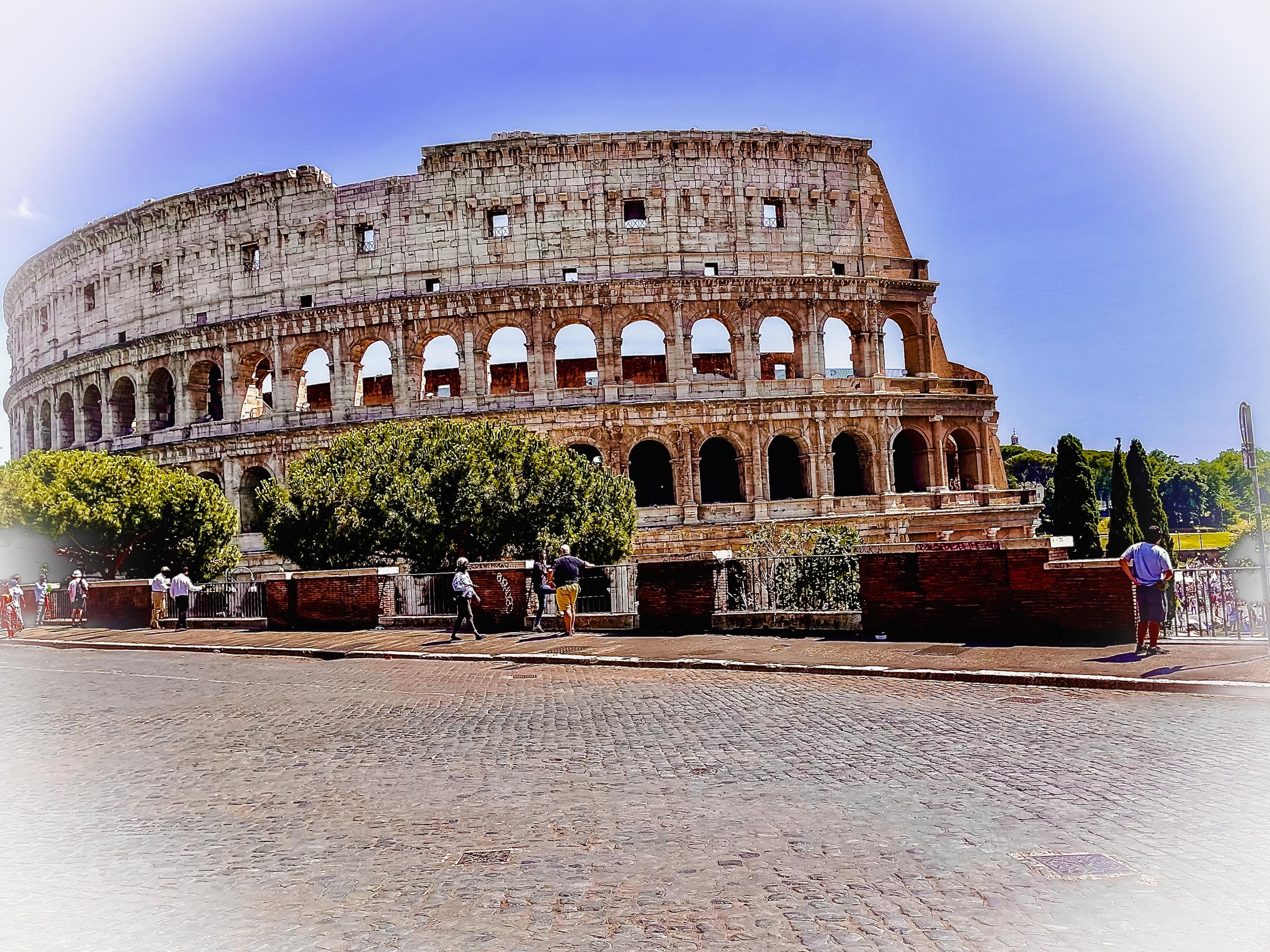 The Colosseum, an ancient Roman amphitheater, with tourists walking nearby on a sunny day.