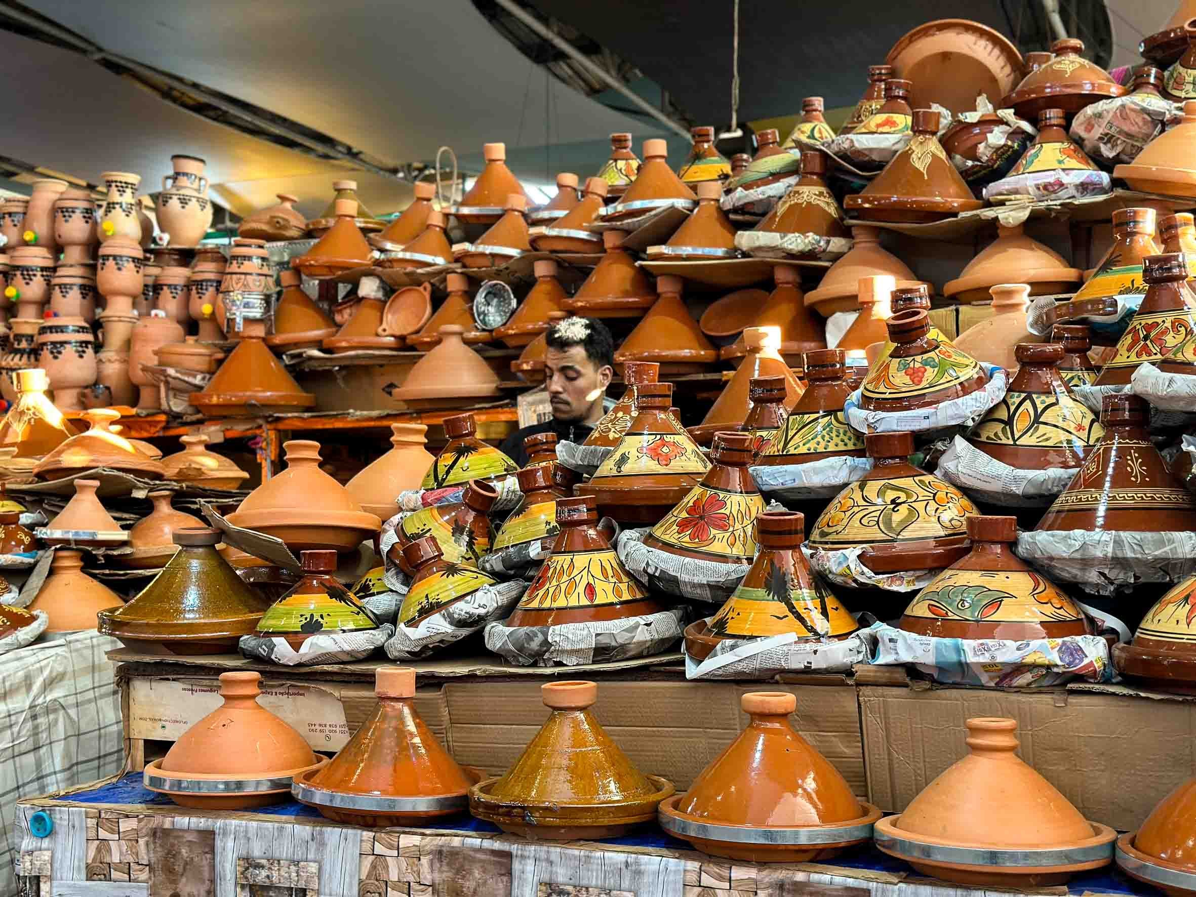 A market stall displaying a variety of colorful, traditional Mexican pottery, including sombrero-shaped decorative items in orange terracotta and painted designs, with a man browsing the items.