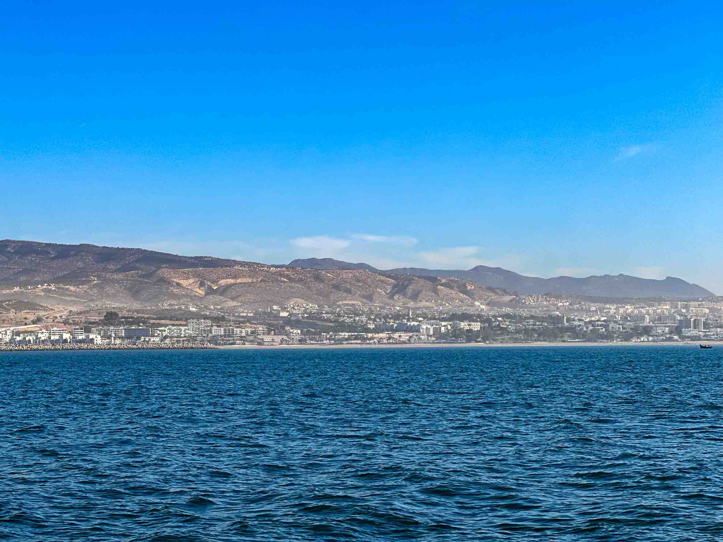 View of a large body of water with a city and hills in the background under a clear blue sky.