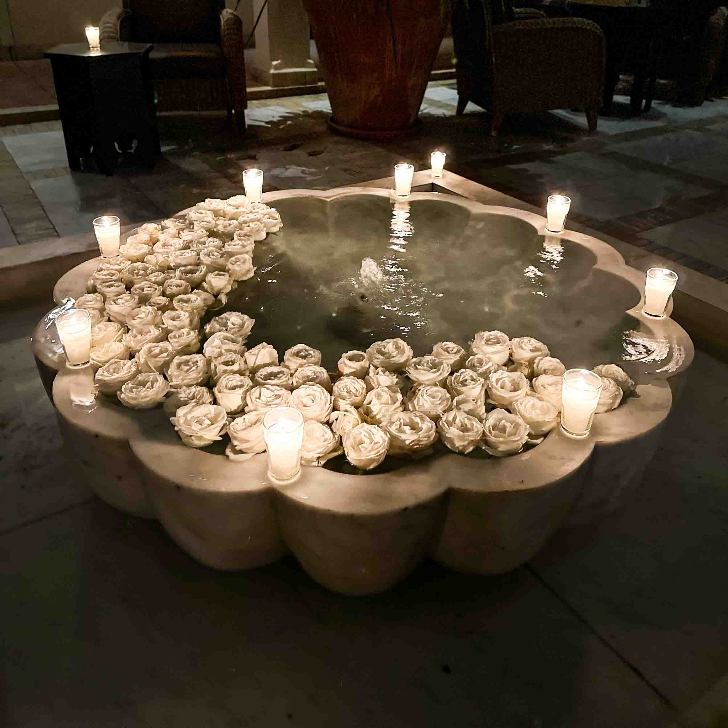 A decorative fountain surrounded by dozens of white roses and lit candles for a romantic or special occasion.