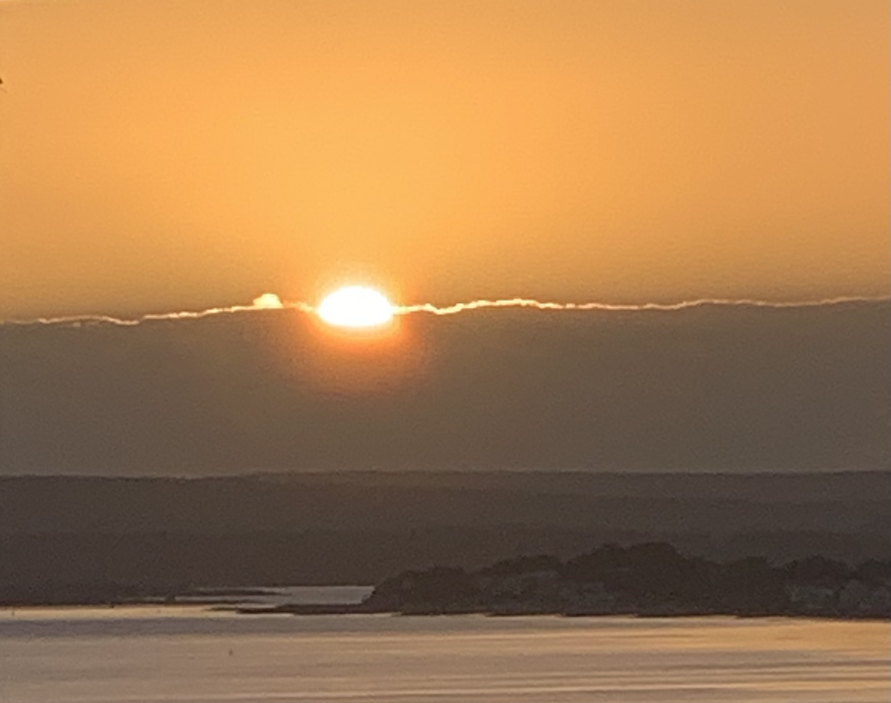 Sunset over a calm body of water with silhouetted hills or rocks in the foreground.