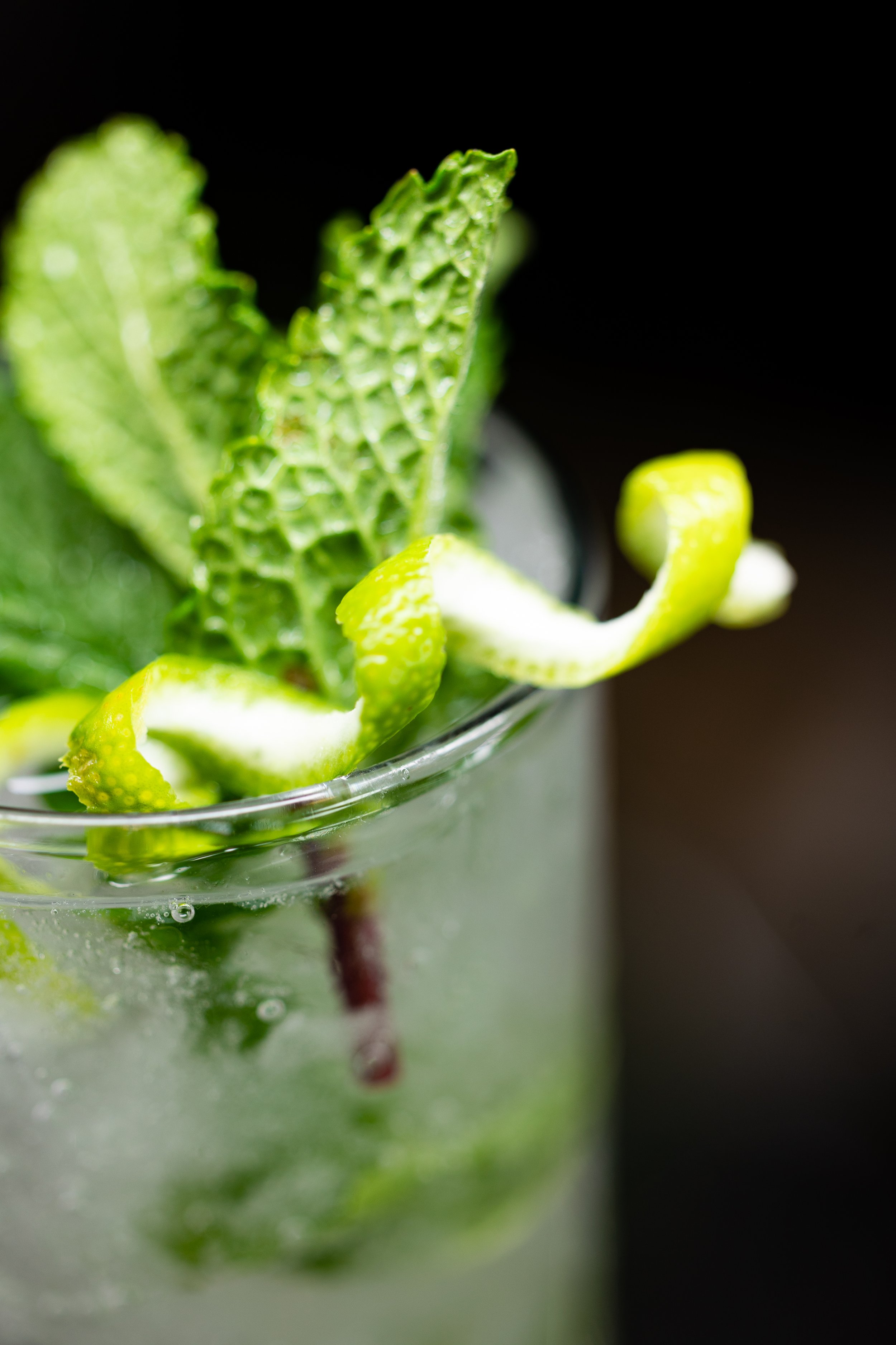 Close-up of a lime and mint garnish in a glass of cocktail with bubbles and a dark background.