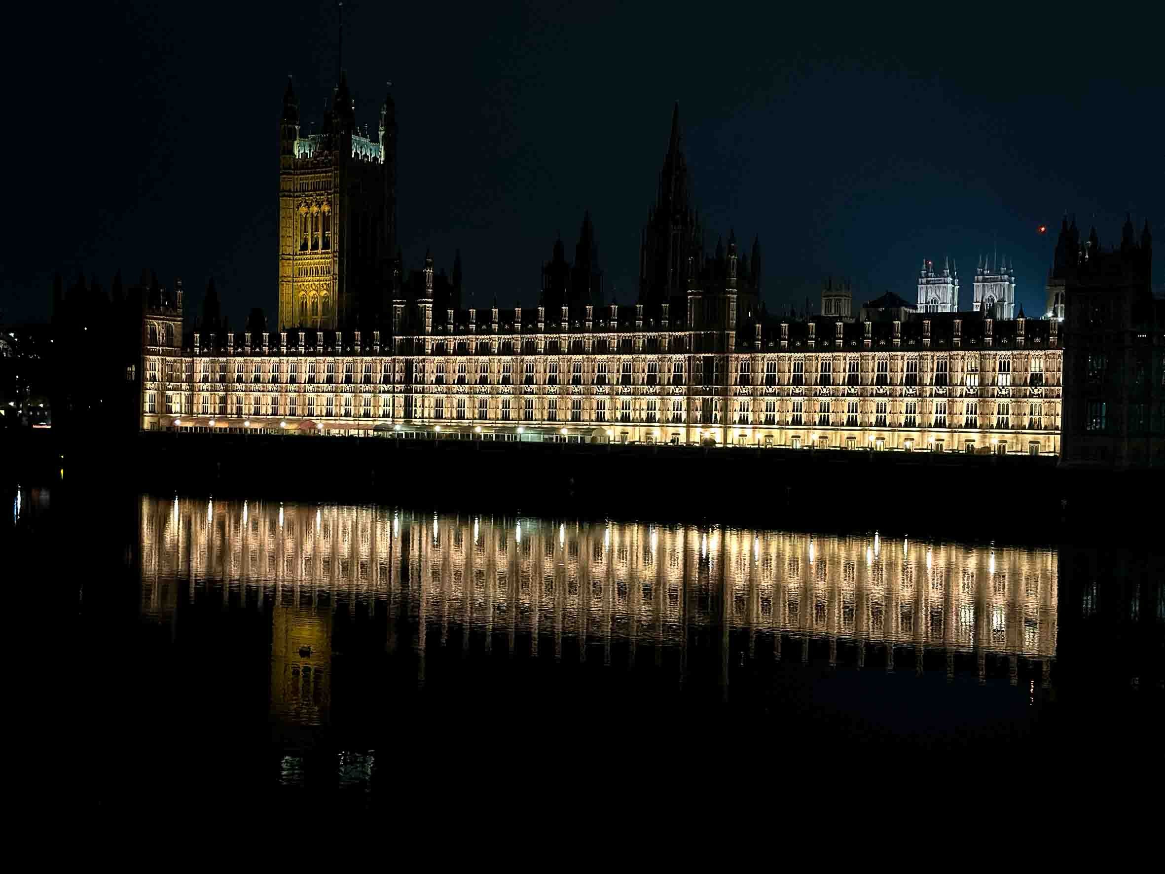 Night view of illuminated Palace of Westminster with reflections on the river.