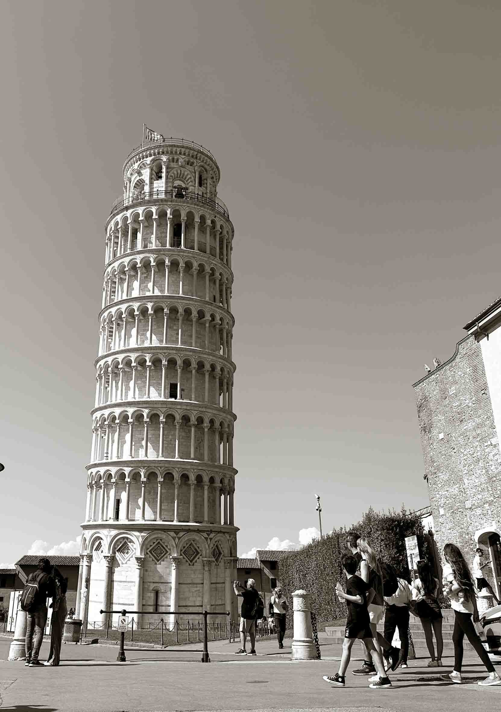 Black and white photo of the Leaning Tower of Pisa with tourists walking and taking pictures in front.