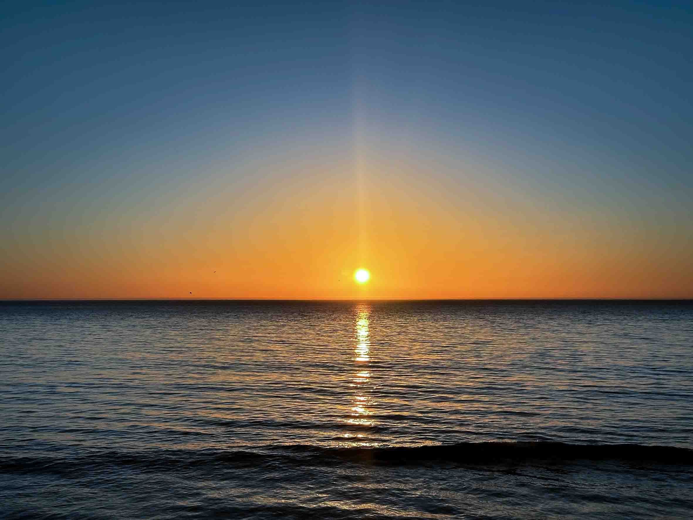 Sunset over the ocean with calm waves and a clear sky.