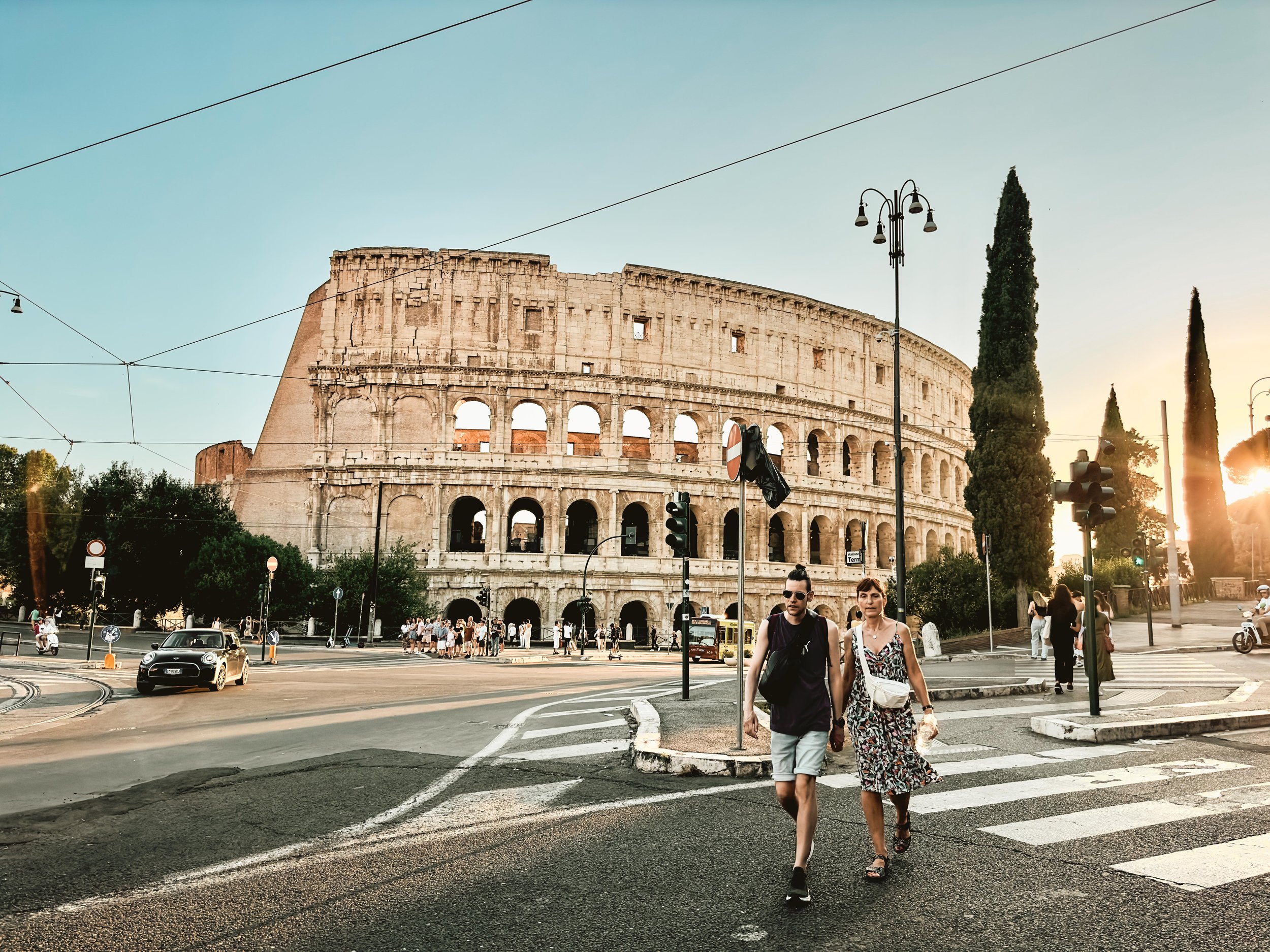 Tourists crossing the street in front of the Colosseum in Rome at sunset.