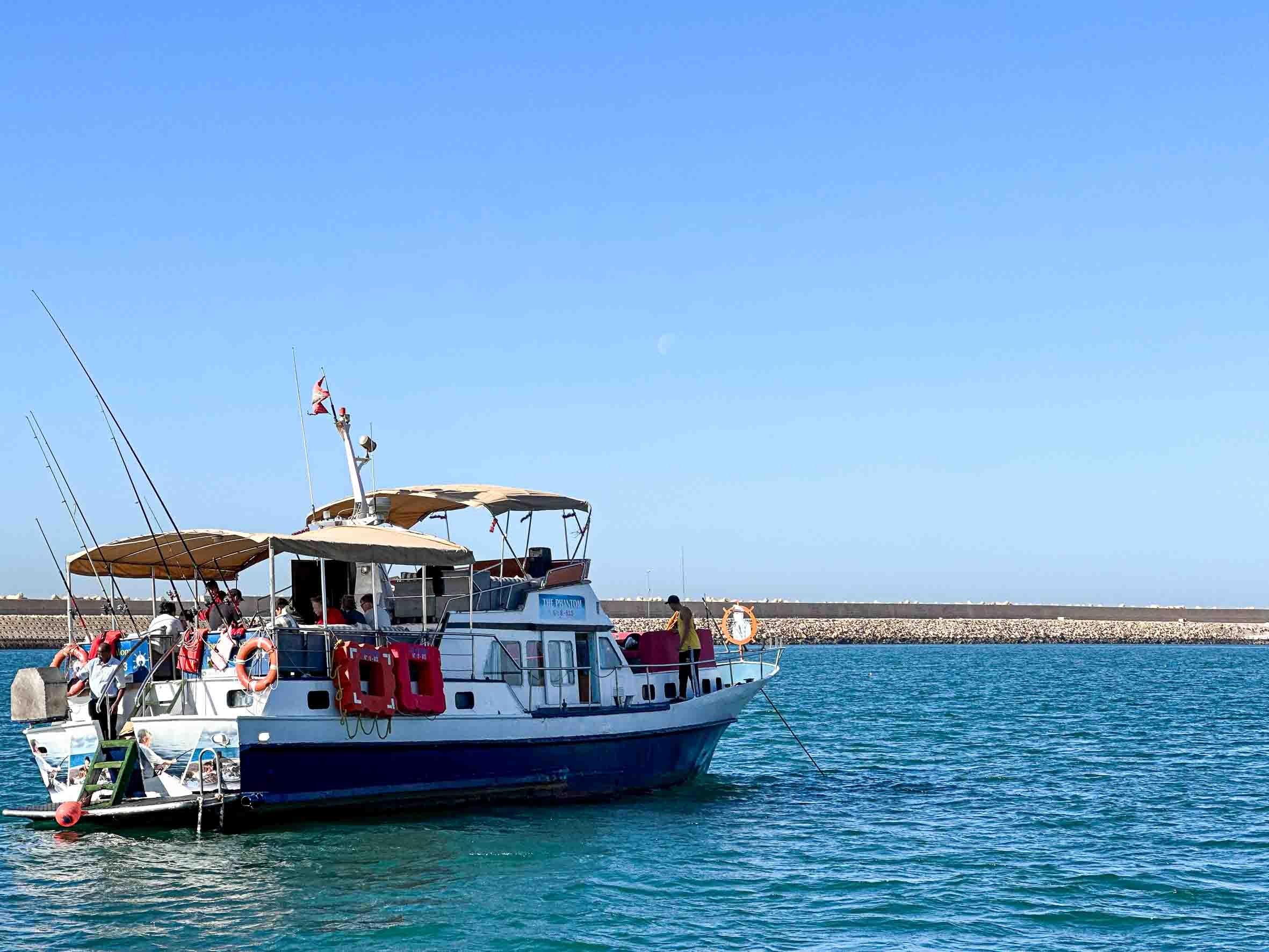 A white and blue boat docked at a marina with several people on board, under a clear blue sky.