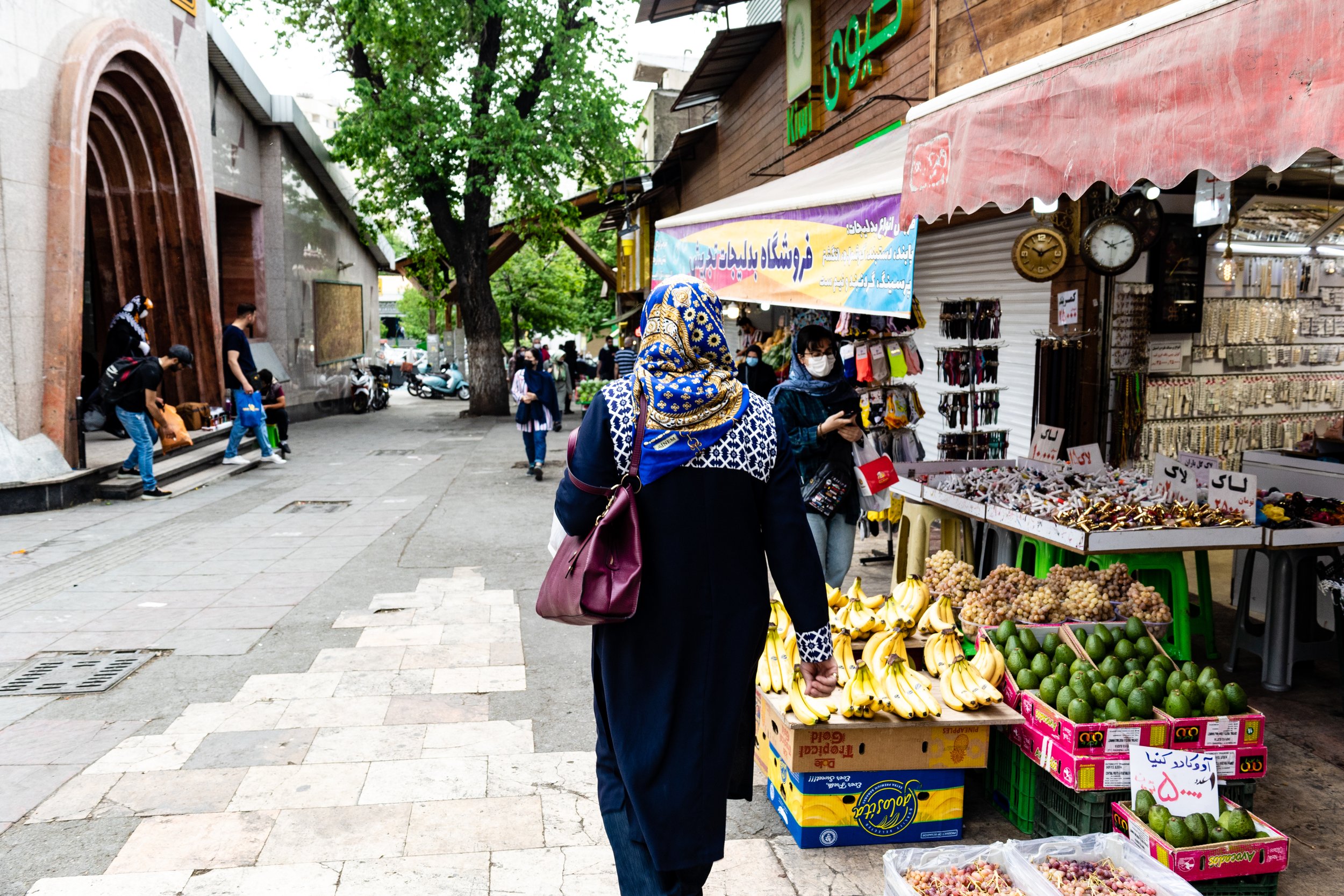 Woman with a headscarf shopping for bananas and avocados at an outdoor street market
