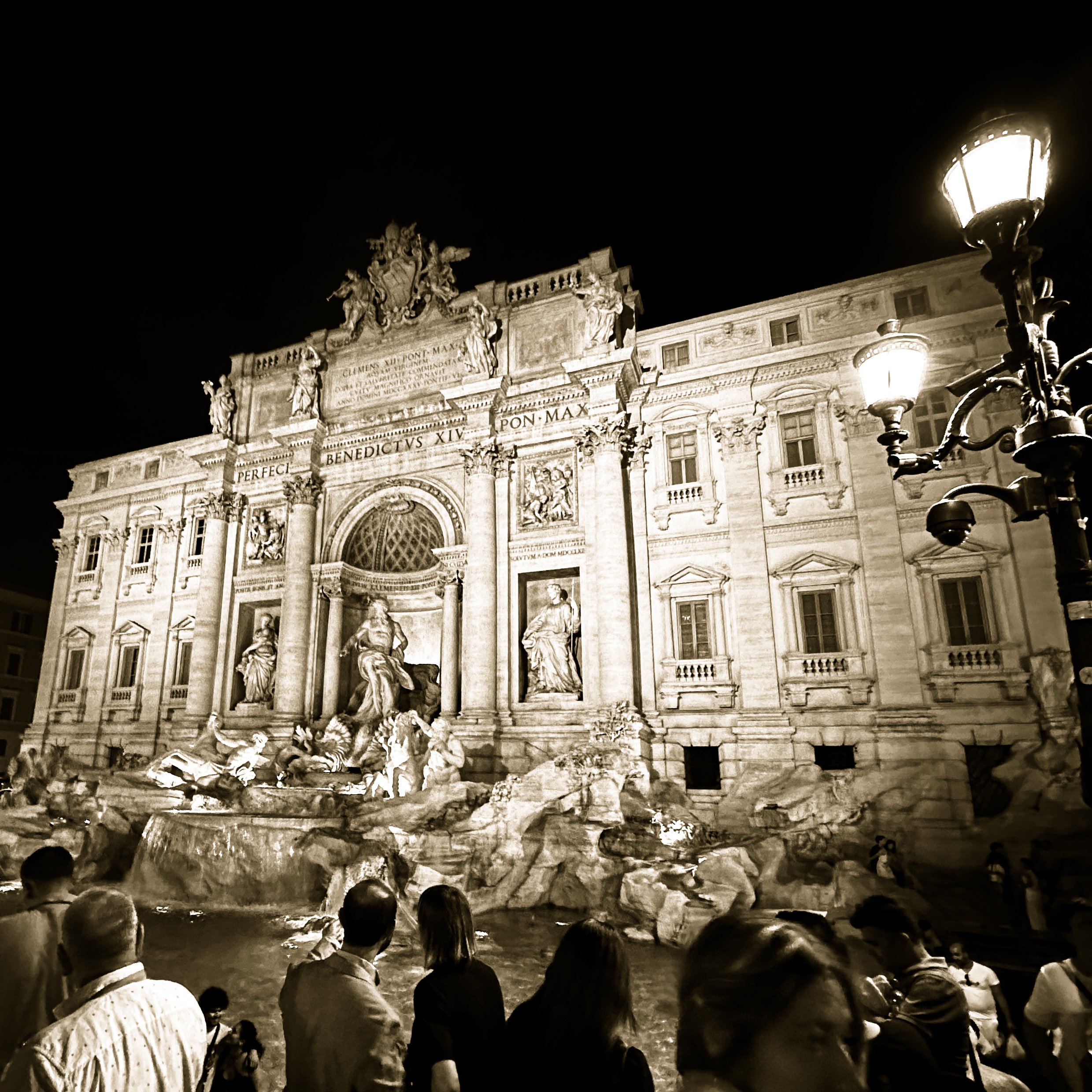 Night view of the Trevi Fountain in Rome, Italy, illuminated with people standing in front.