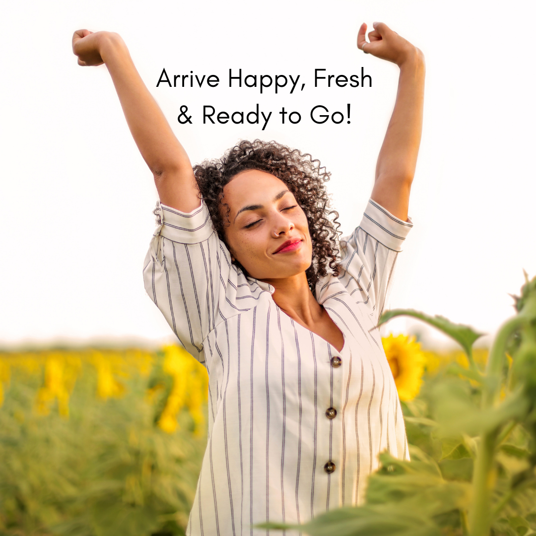 A woman with curly hair and a striped shirt standing in a sunflower field with her eyes closed and arms raised in a victorious pose, smiling. The text overlay reads, "Arrive Happy, Fresh & Ready to Go!"