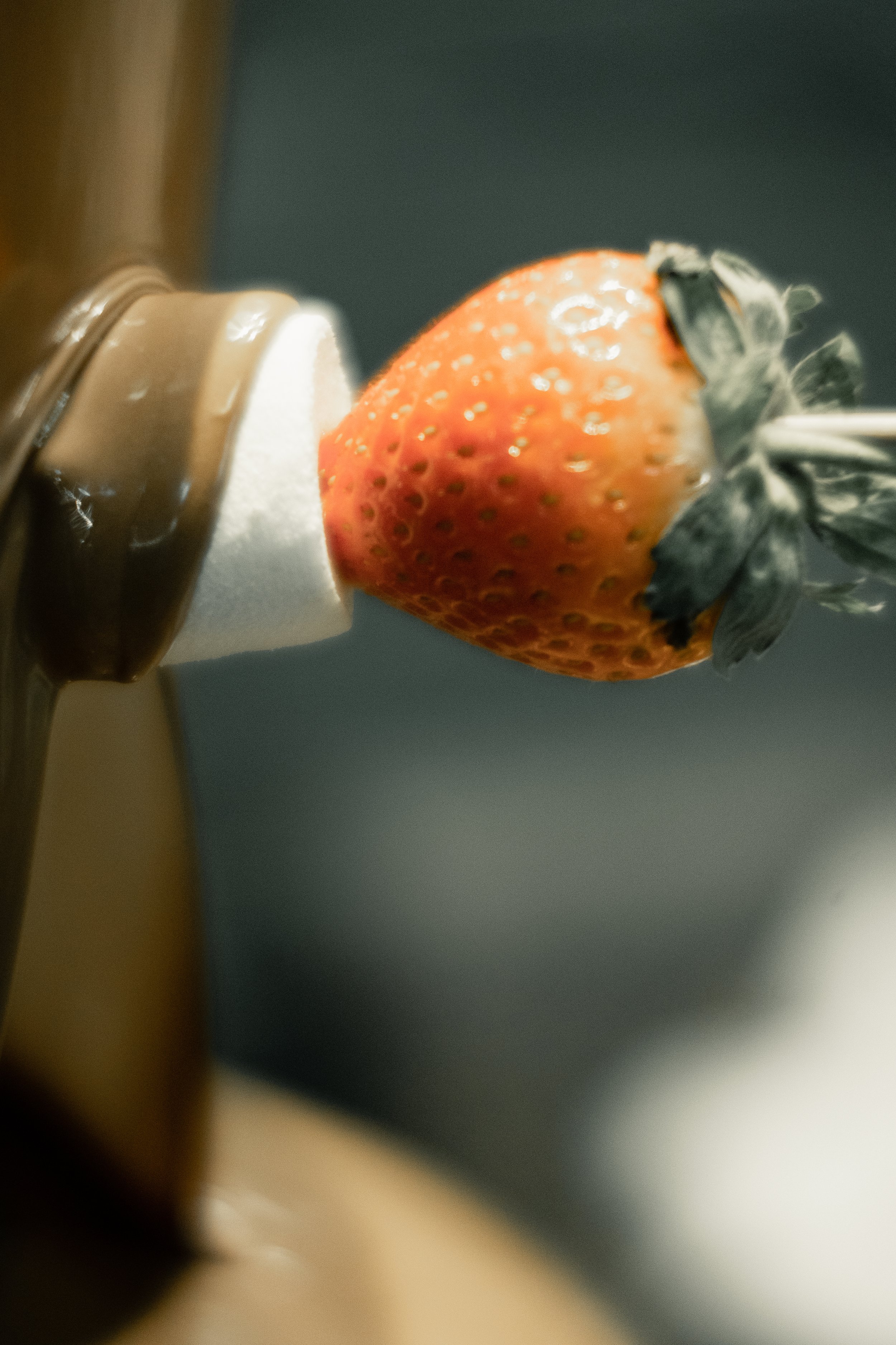 Close-up of a strawberry being dipped in chocolate on a stick.