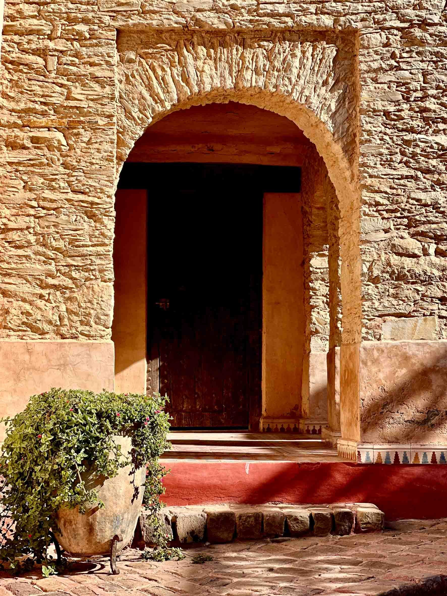 Stone building with an arched doorway and a potted plant in front