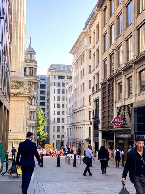 City street with people walking, tall buildings, and a London Underground sign.
