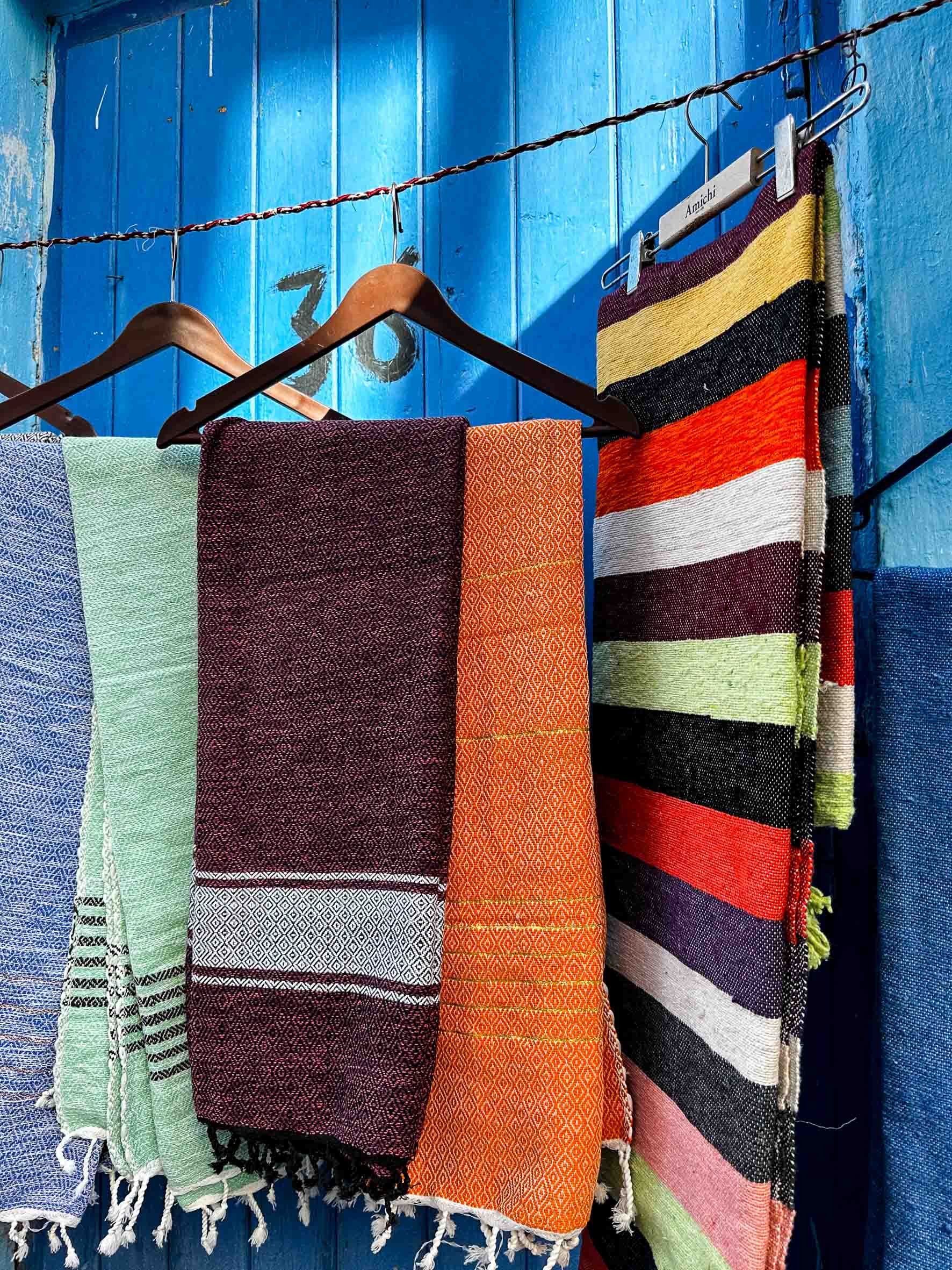 Colorful woven textiles hanging on a blue wooden wall.