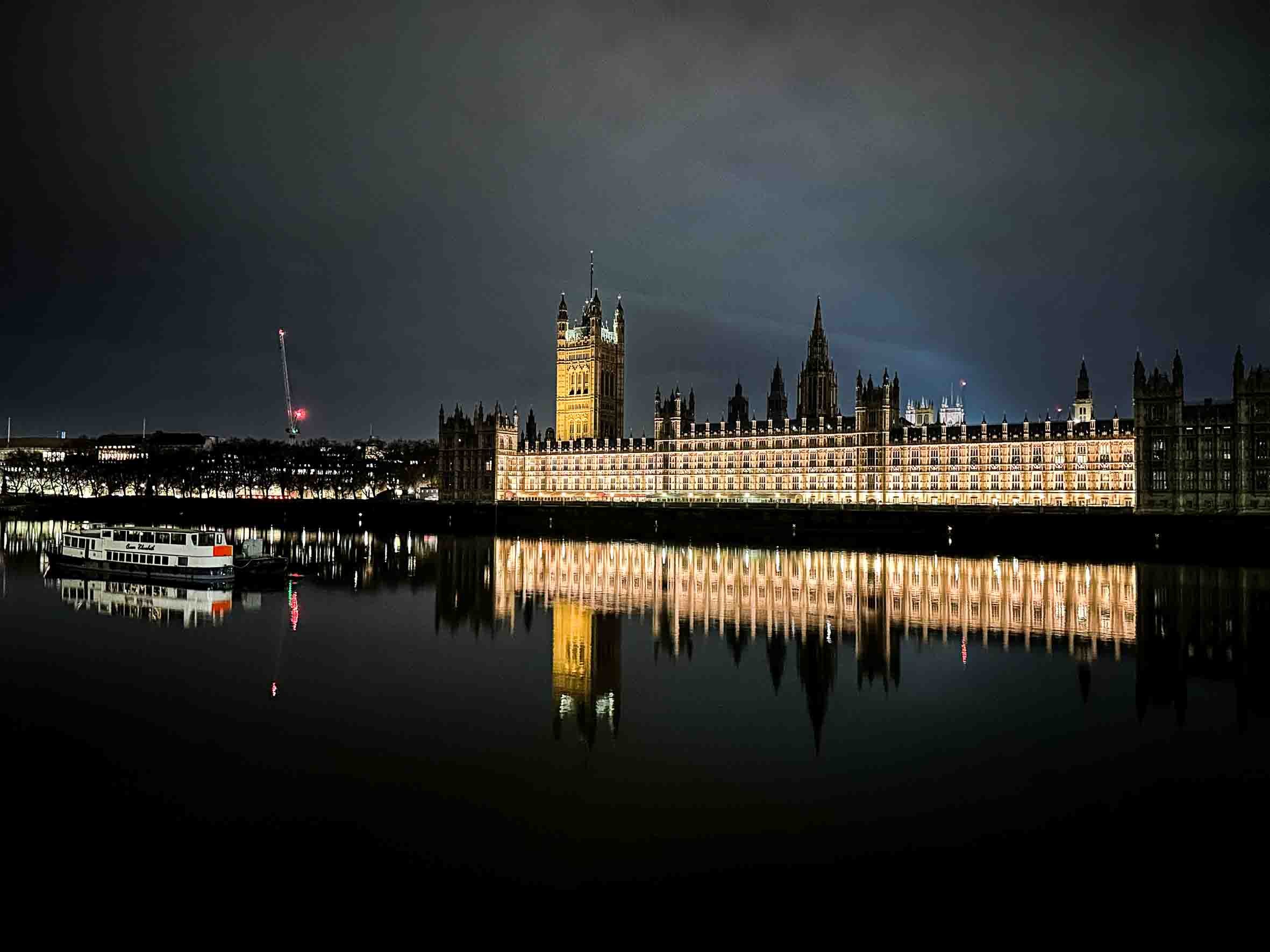 Night view of the illuminated Palace of Westminster and Big Ben reflected in the River Thames in London.