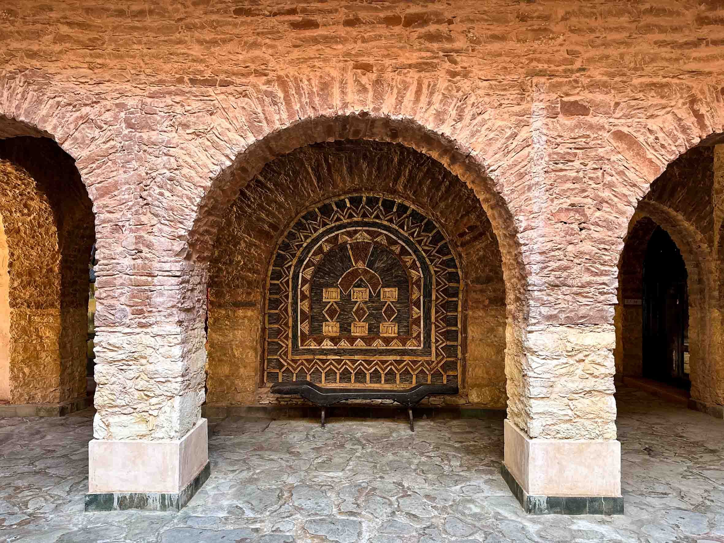 Stone archways with a decorative wooden panel and a black bench underneath.