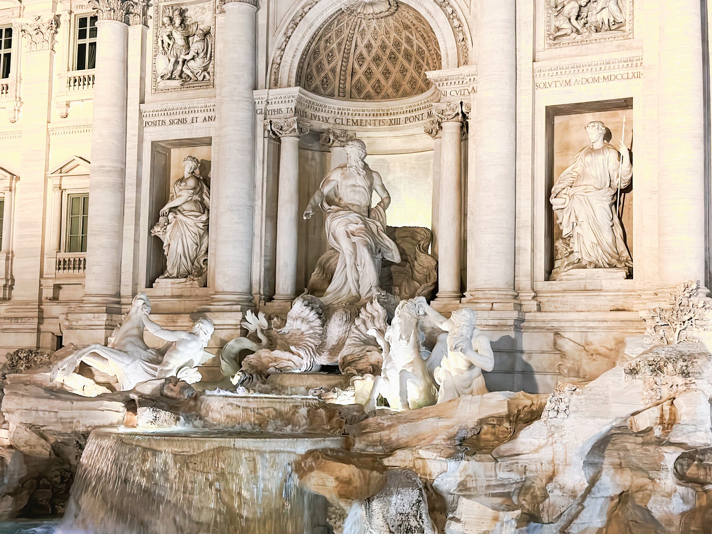 The Trevi Fountain in Rome at night, illuminated, with detailed sculptures and cascading water.