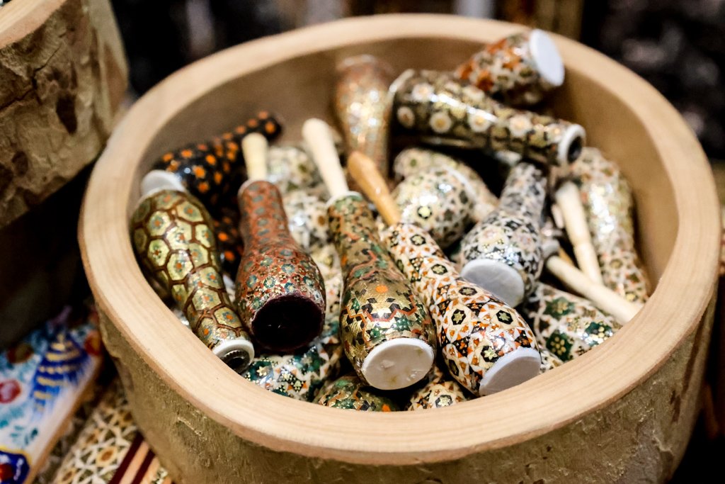A wooden bowl filled with decorative mosaic thimbles with intricate colorful patterns