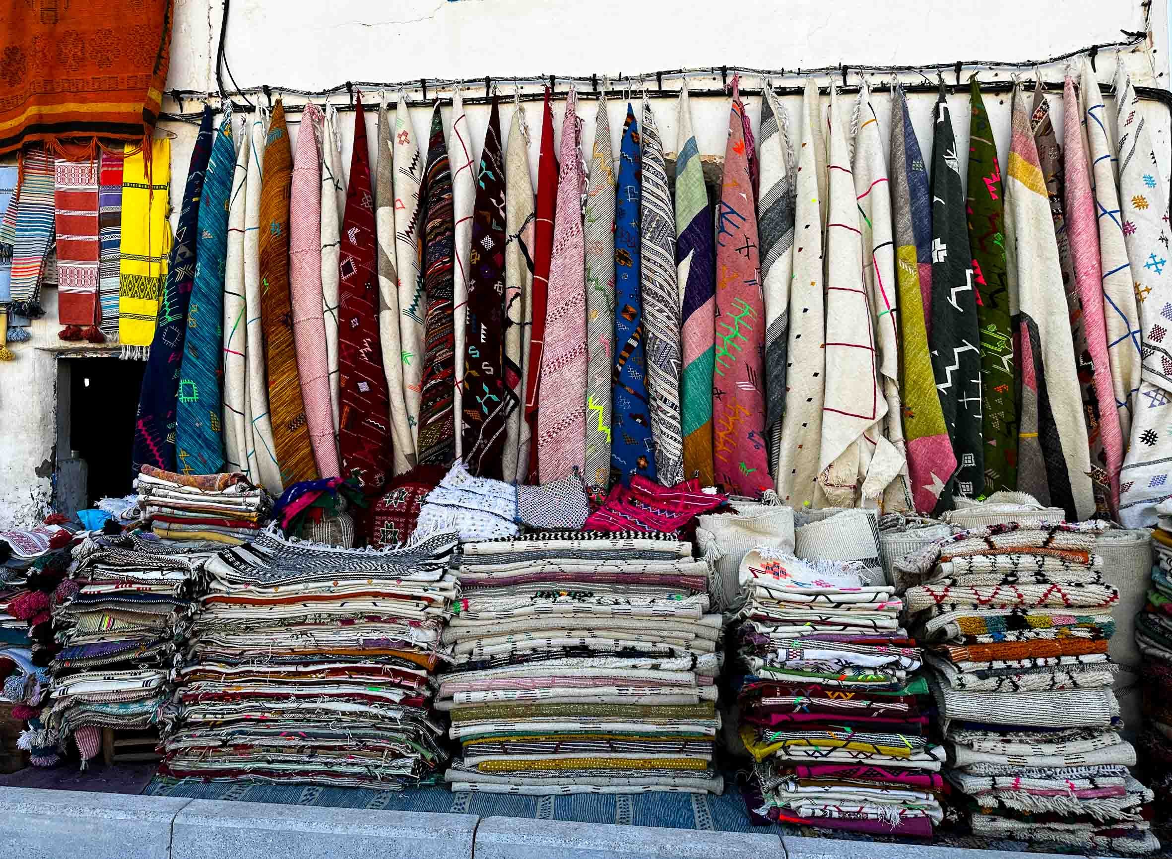 Colorful traditional woven textiles with various patterns and designs displayed on a storefront