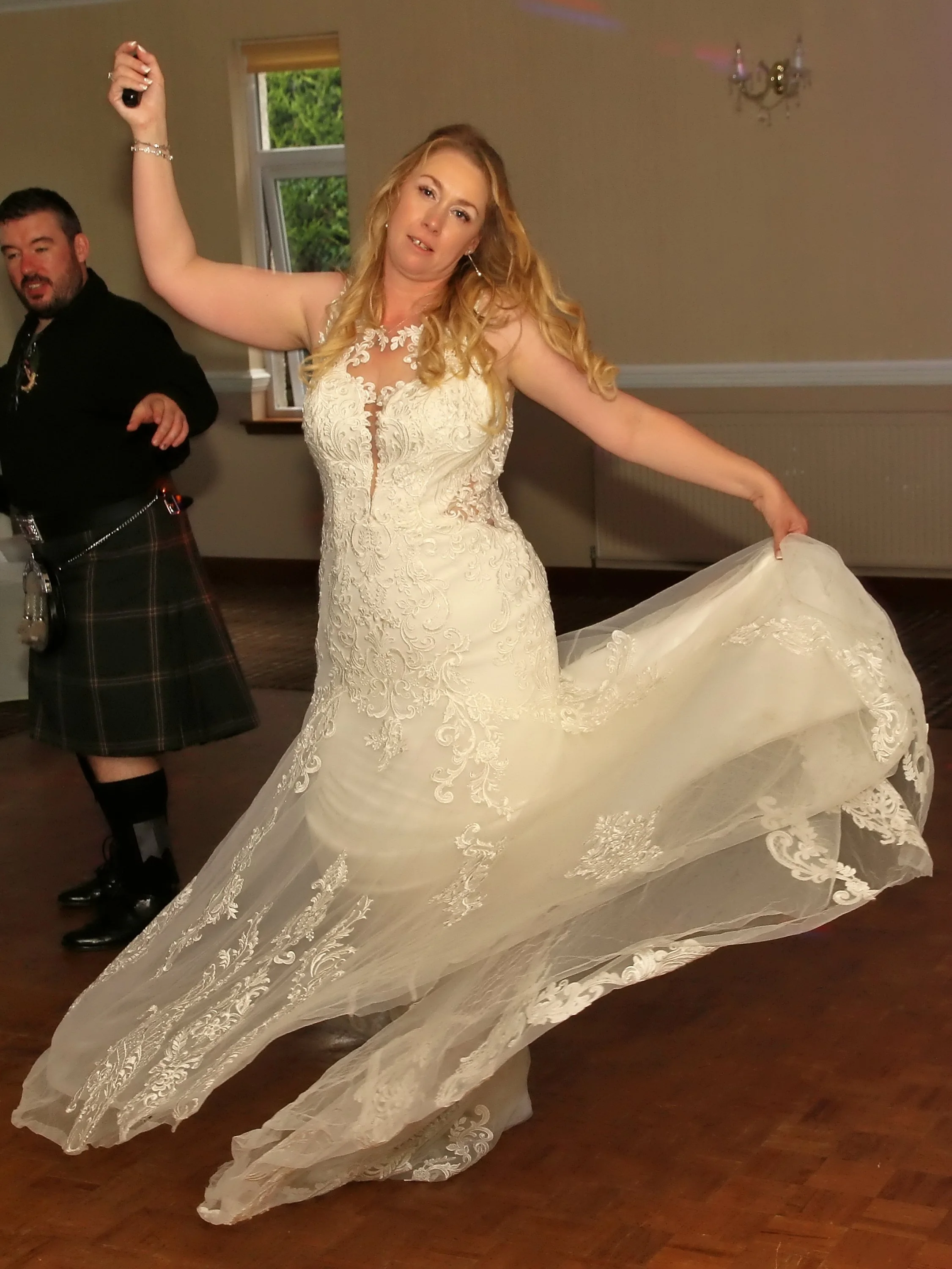 Woman in a wedding dress dancing with a man in a kilt at a celebration or wedding reception.