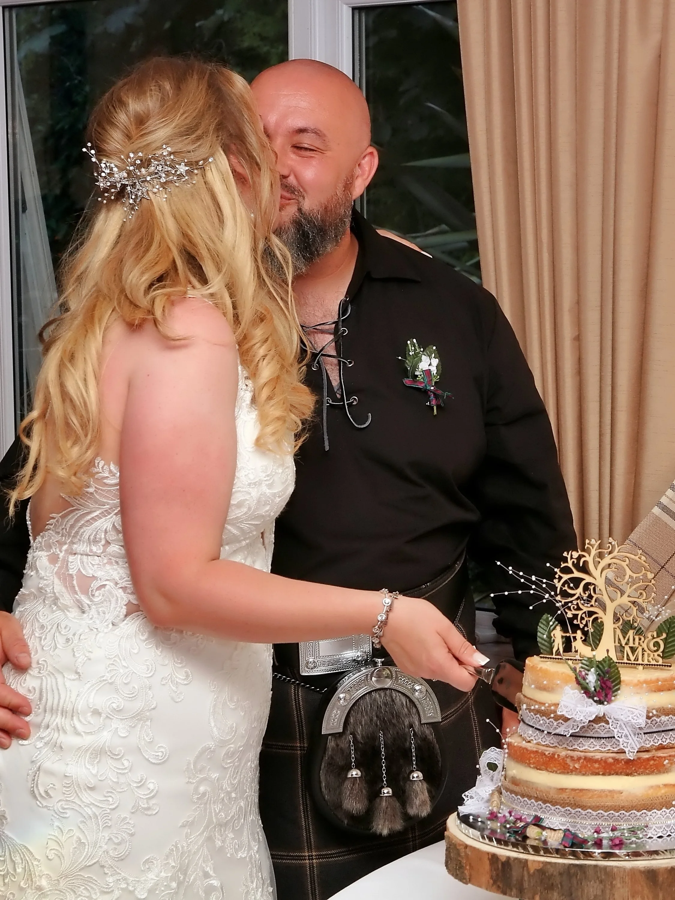 Bride and groom sharing a kiss during wedding celebration, with a decorated cake nearby.