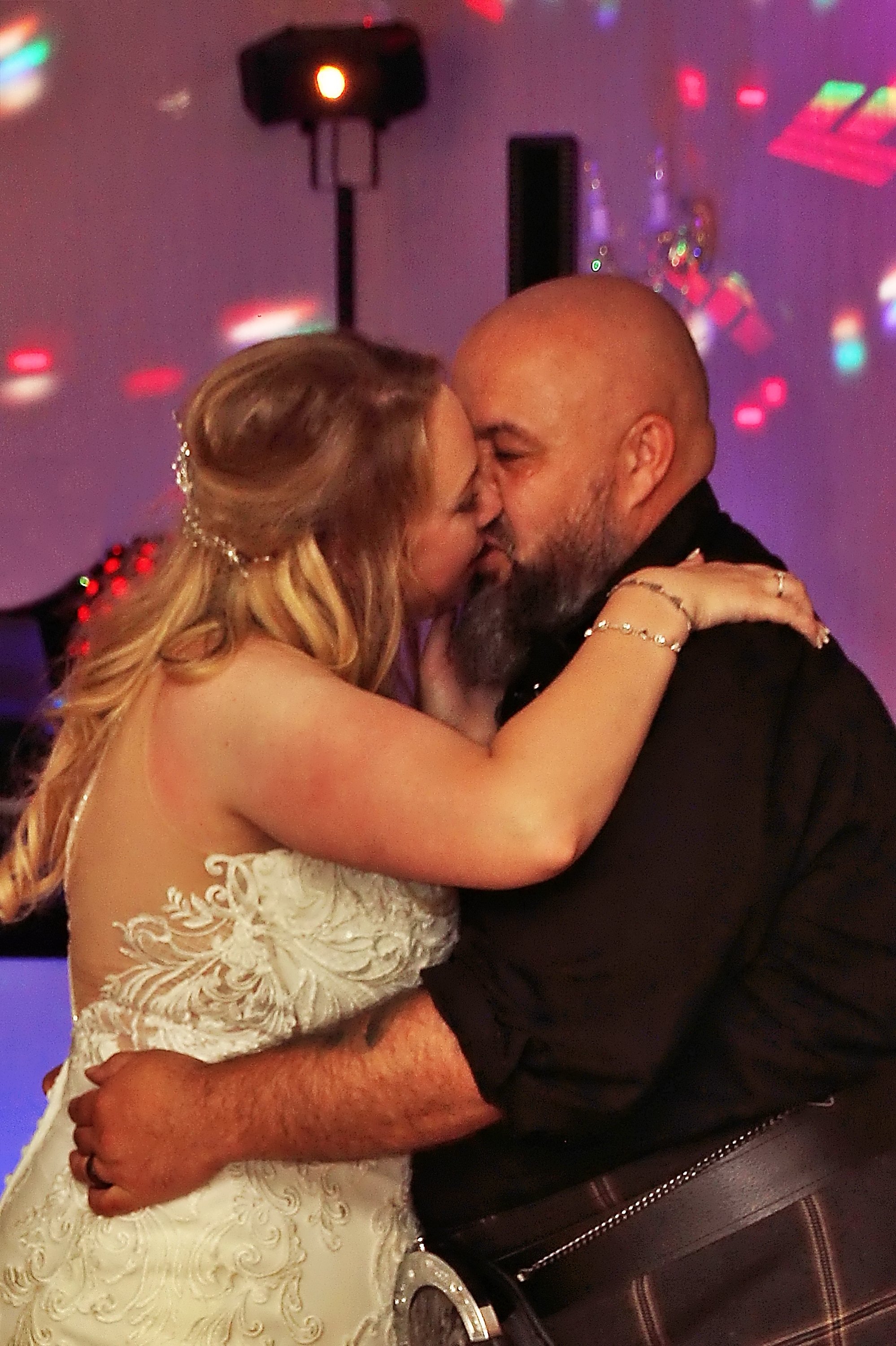 A bride and groom dancing closely at their wedding reception, sharing a kiss.
