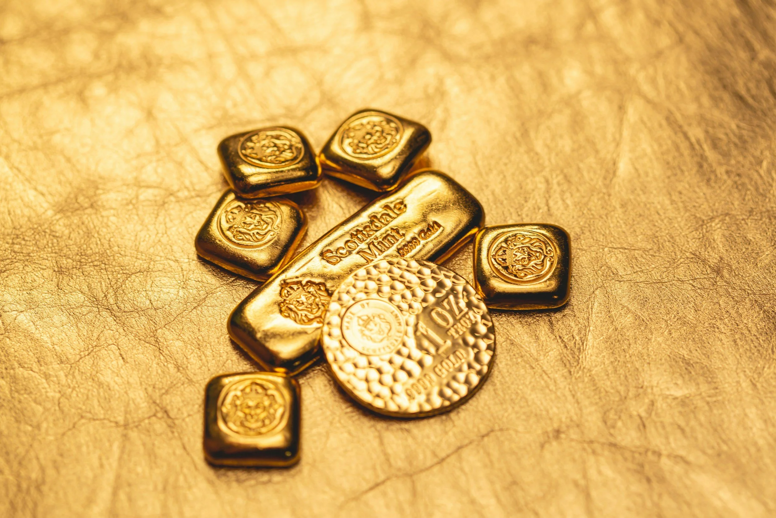 Gold bars, a gold coin, and gold nuggets on a textured gold surface.