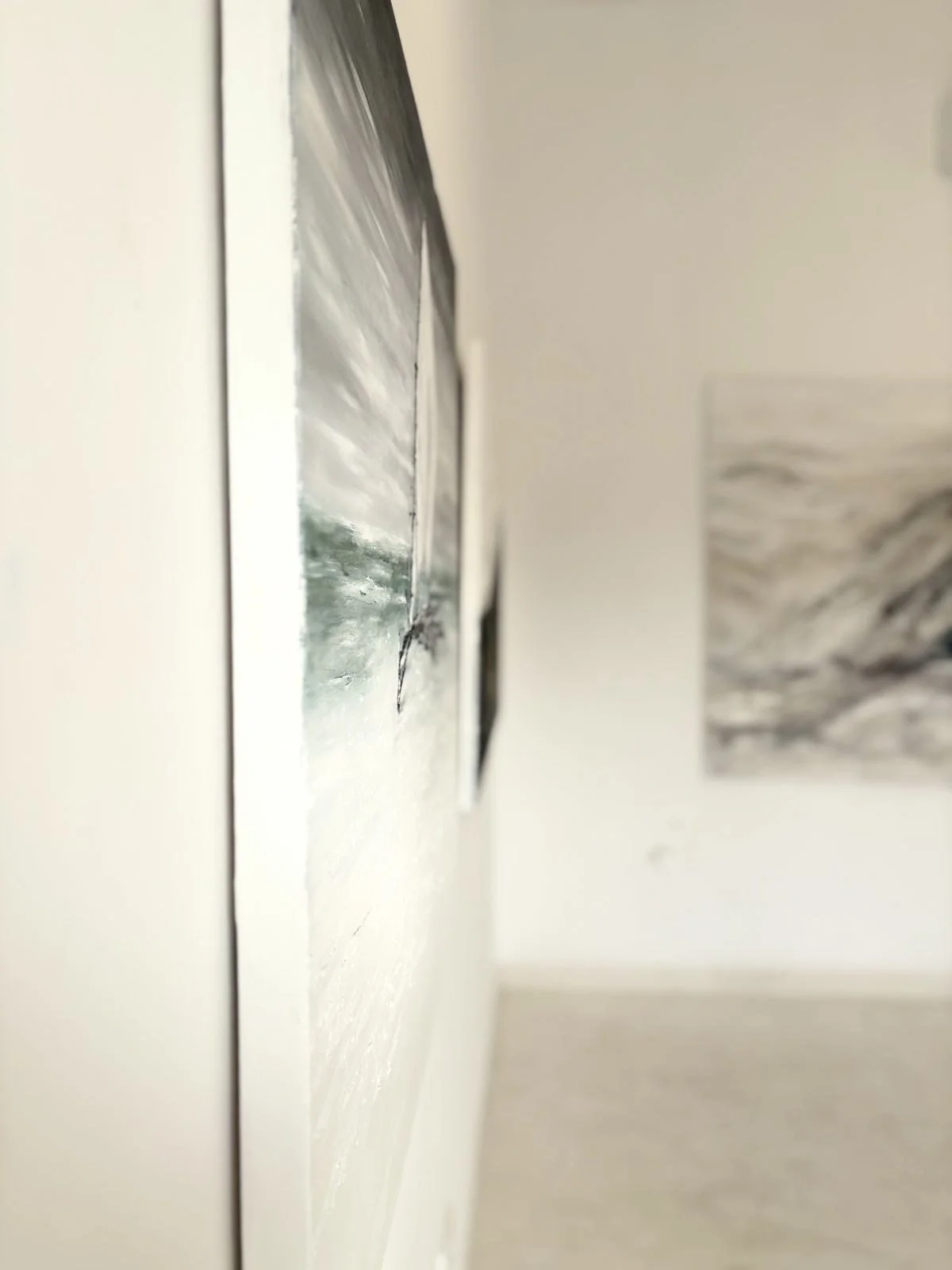 Close-up of an art painting on a wall, with another painting visible in the background, in a gallery setting.