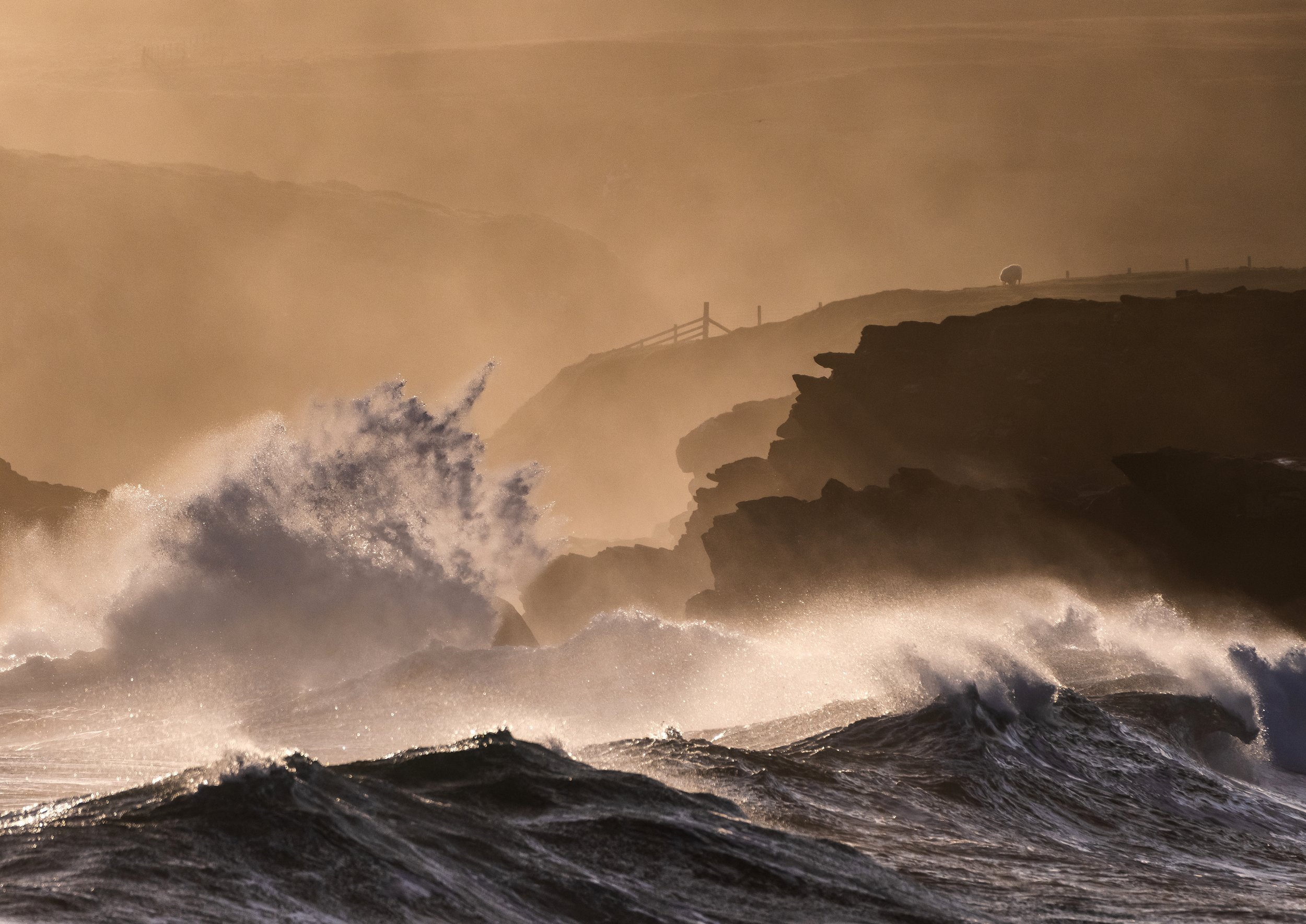 Port of Ness at sunrise on the Isle of Lewis, with towering Atlantic waves crashing into the rocks under warm morning colour.