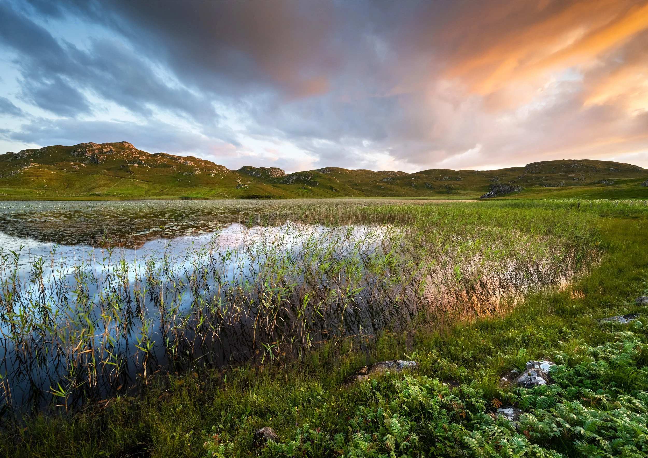 Sunset over Dalbeg Loch on the Isle of Lewis, with pink and orange tones in the sky mirrored on the calm surface.