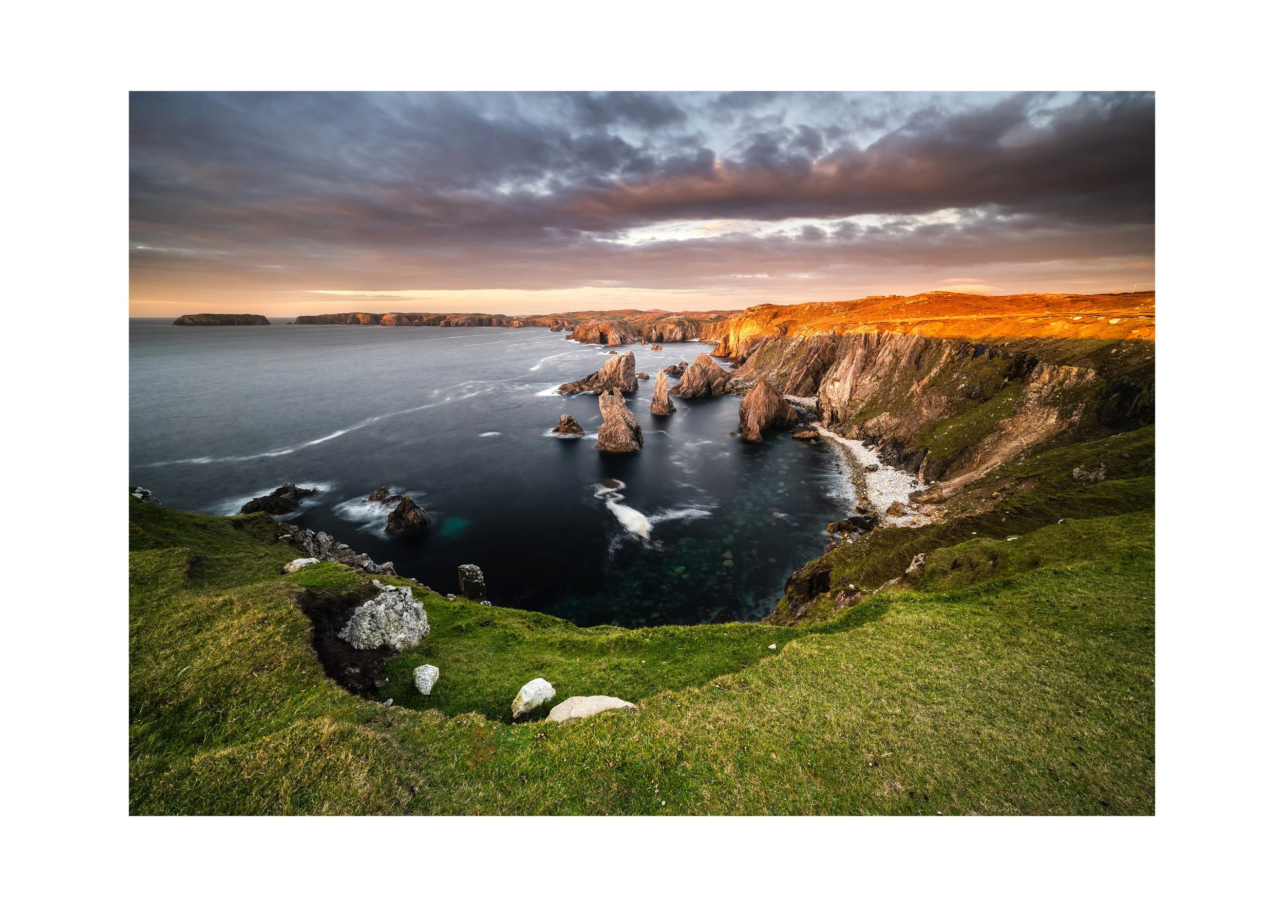 Mangersta sea stacks at sunset on the Isle of Lewis, with warm light on the cliffs and Atlantic waves moving through the bay.