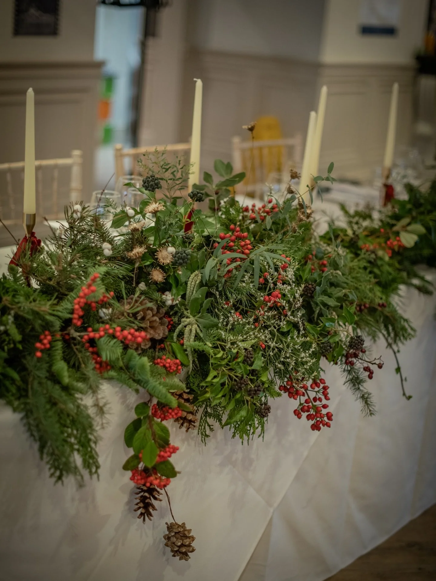 12 ft of luscious tumbling evergreens and berries, candles and red ribbon dressing Laura &amp; Wayne&rsquo;s Christmas top table. Created in 7 sections, some of which are now gracing the mantelpieces of L&amp;W and their friends and family. I couldn&