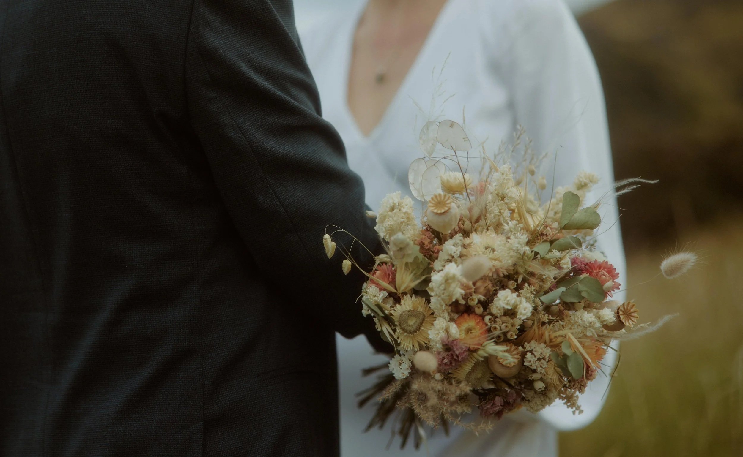 a dried flower bridal bouquet in neutral shades with warm apricot and soft greens. A wild and natural look from the soft grasses and seedheads