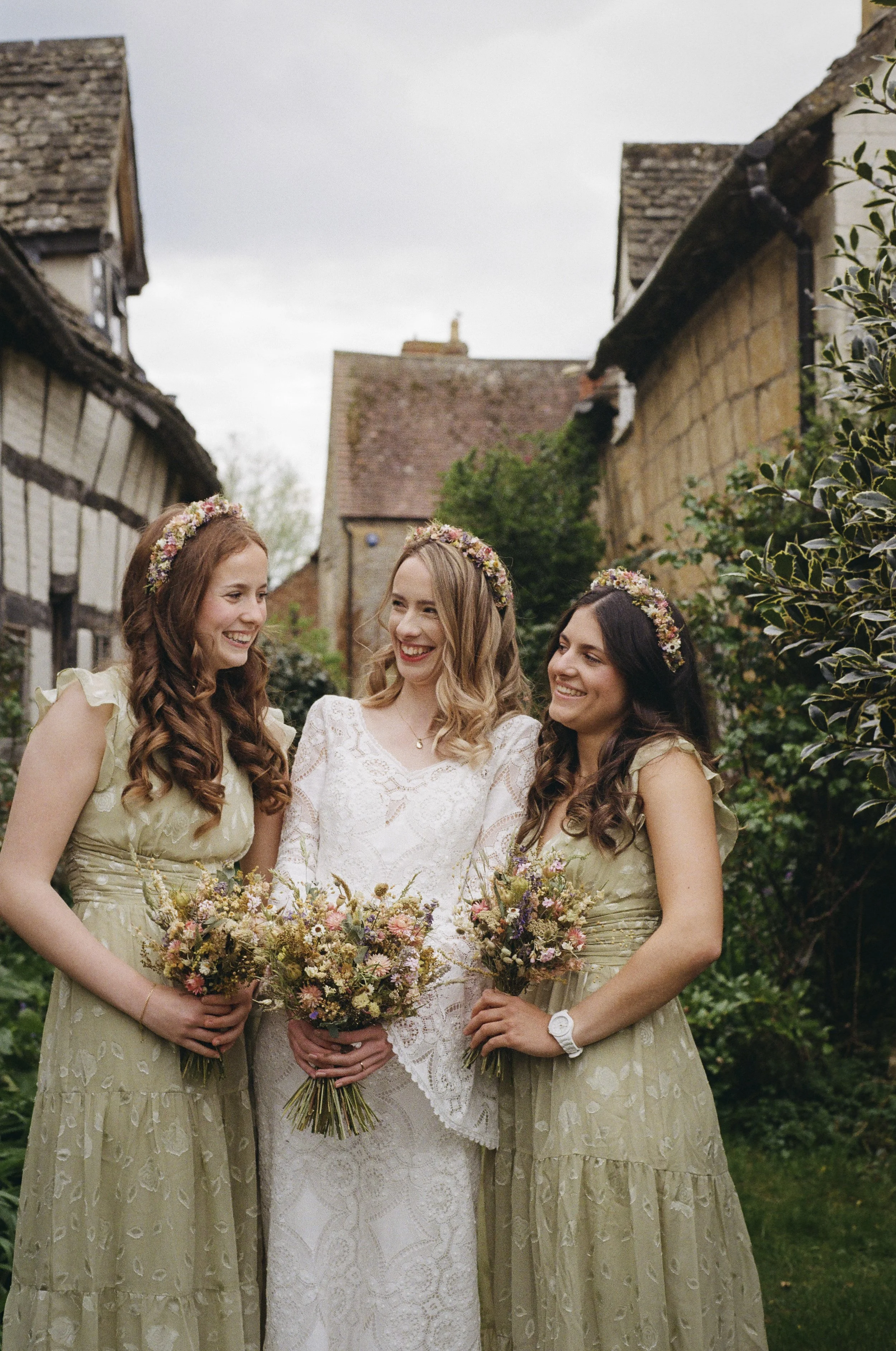 bride and bridesmaids with dried flower bouquets and dried flower headband.  All a very natural, rustic, country feel with soft pastels and wild flower look. Long, vintage style dresses. Backdrop of half-timbered buildings
